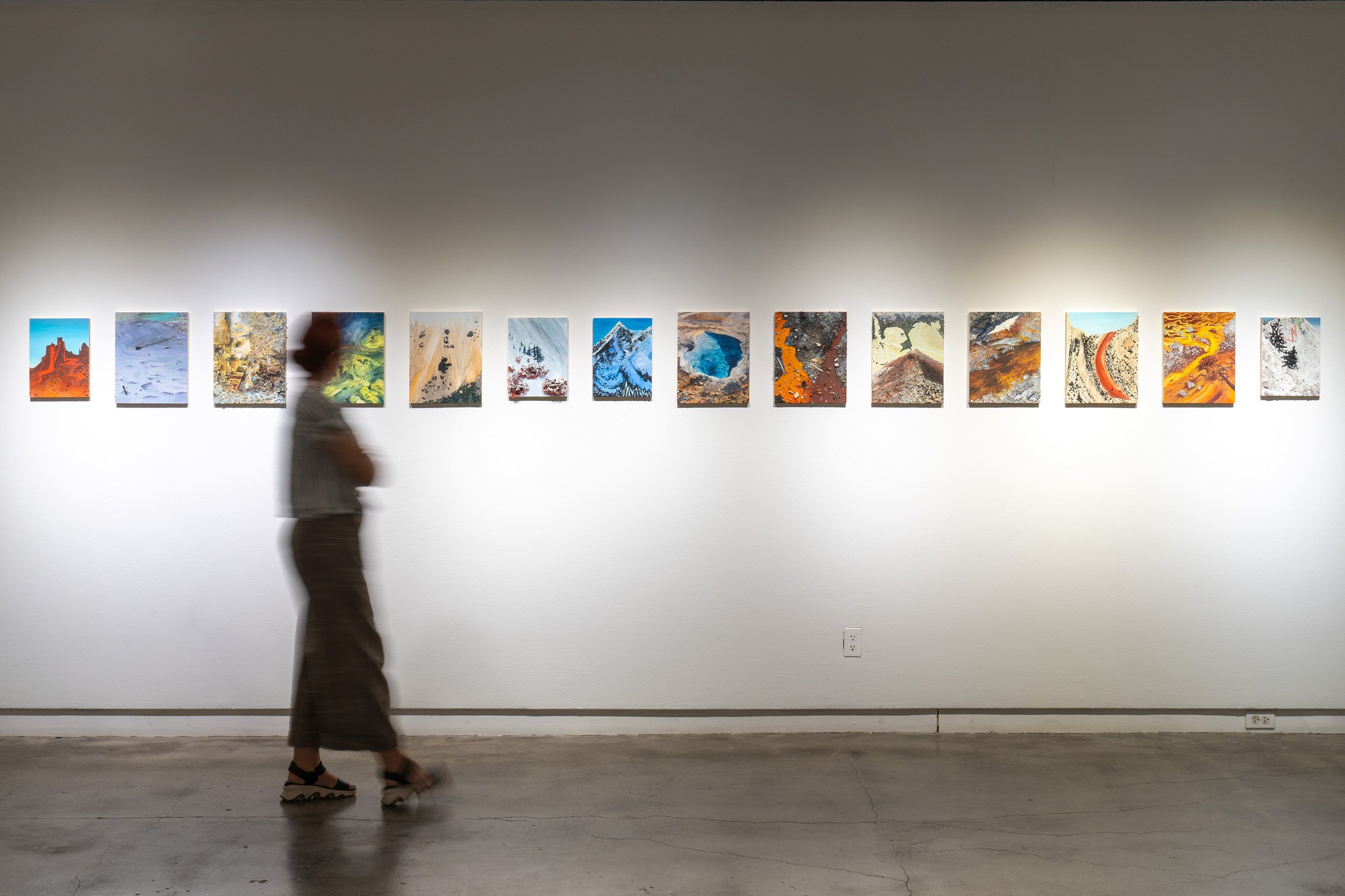 Person walking past a row of colorful abstract paintings in an art gallery.