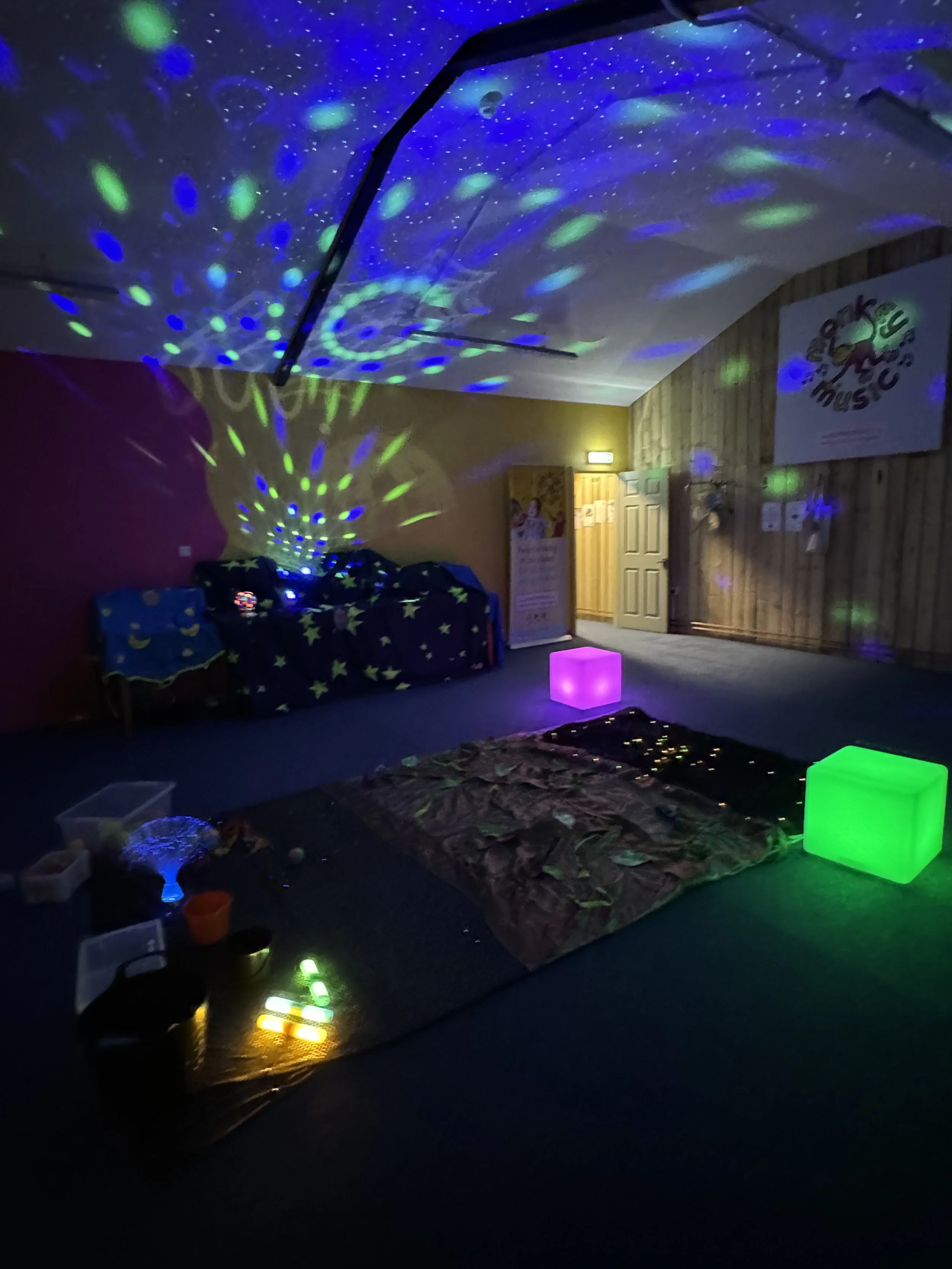 Room with starry light projection, colorful glowing cubes, and illuminated objects on the floor.