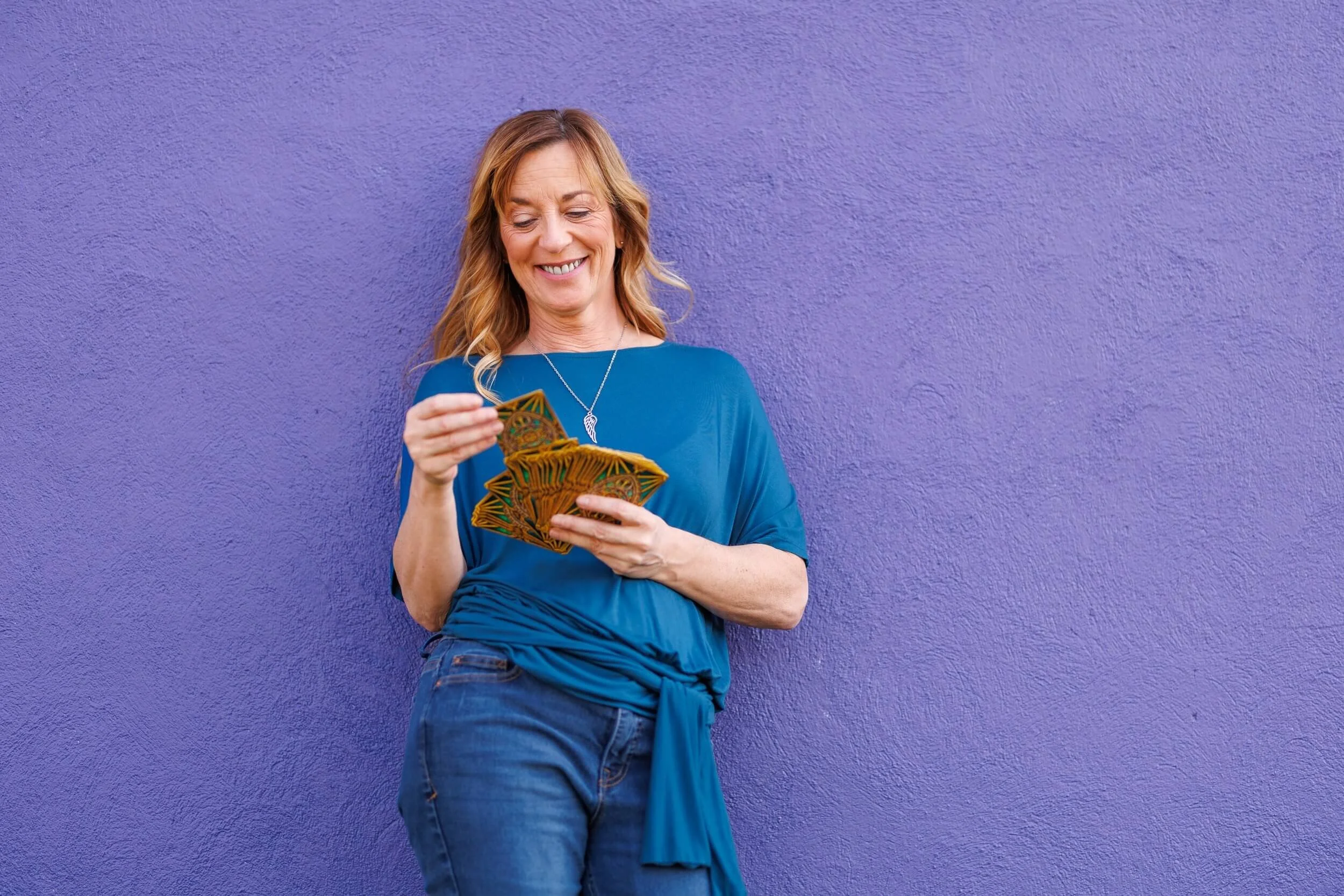 Woman smiling and holding a fan of playing cards standing against a purple wall.