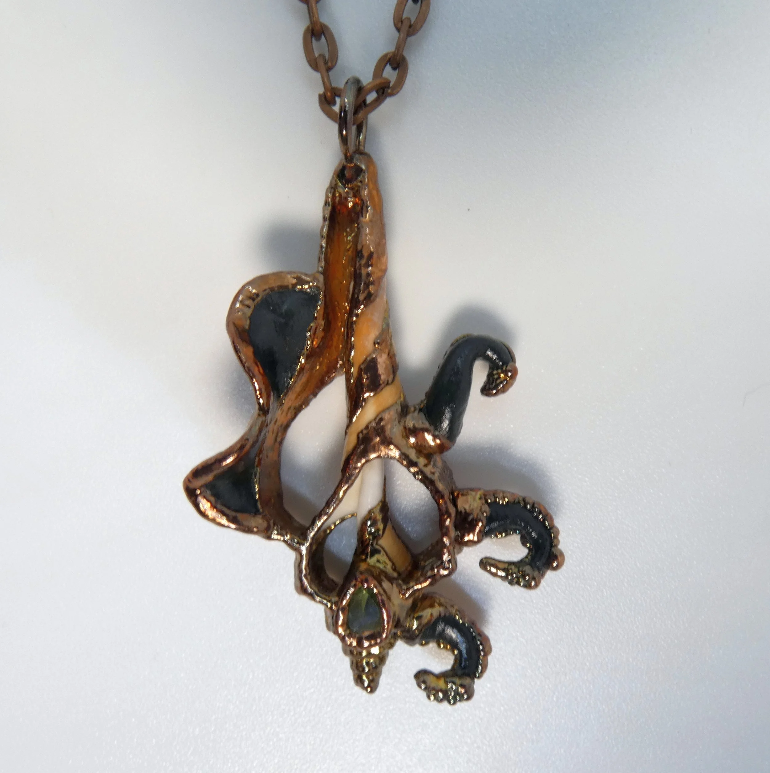 Symbiont 007 (Pendant): seashell slice, faceted peridot, epoxy clay, electroformed in copper. 2.5H x 1.5” W. Available $175.