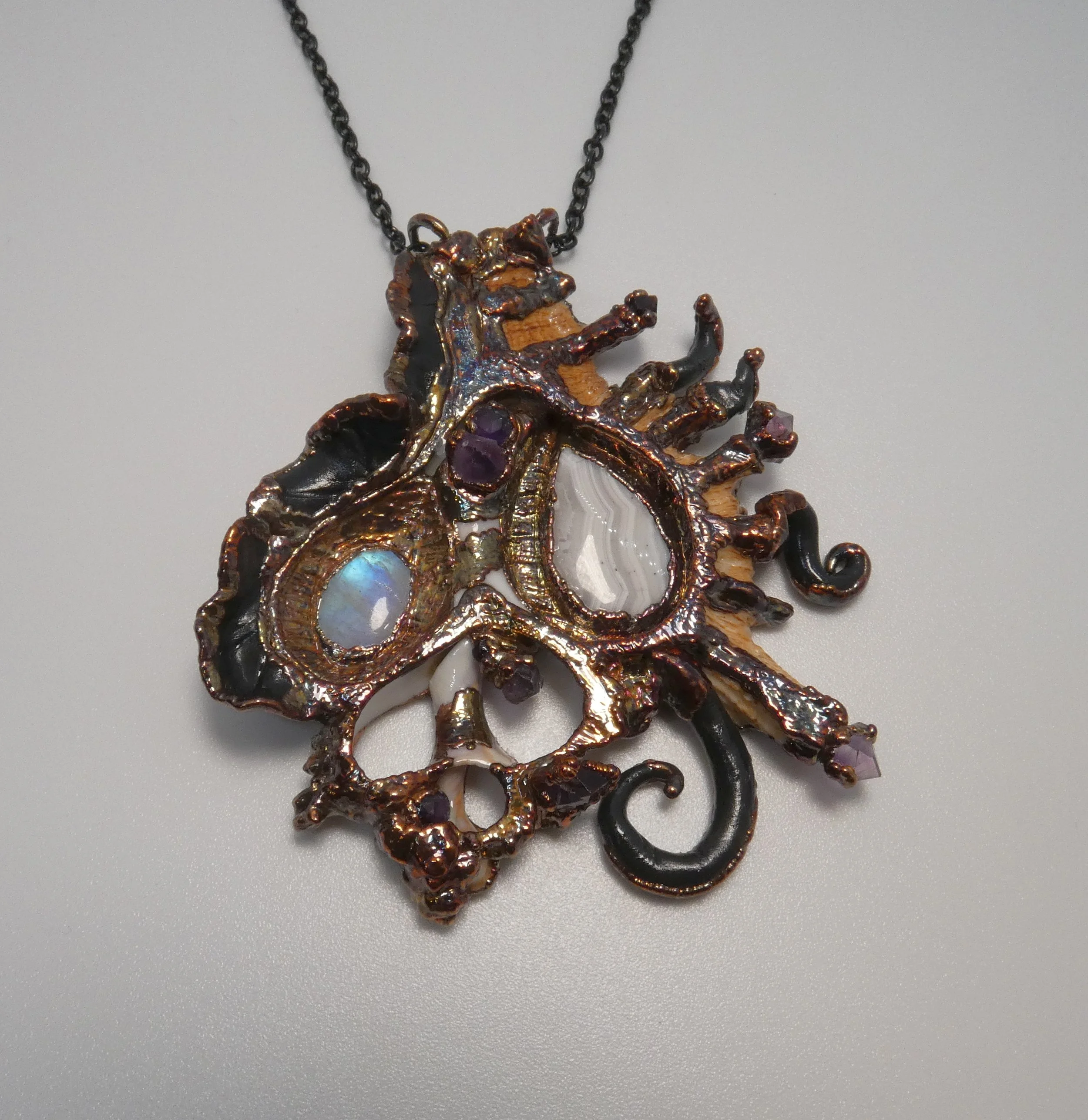 Symbiont 024 (Pendant): seashell slice, lace agate, moonstone, amethyst points, epoxy clay, electroformed in copper. 3” H x 2.75” W. In private collection.