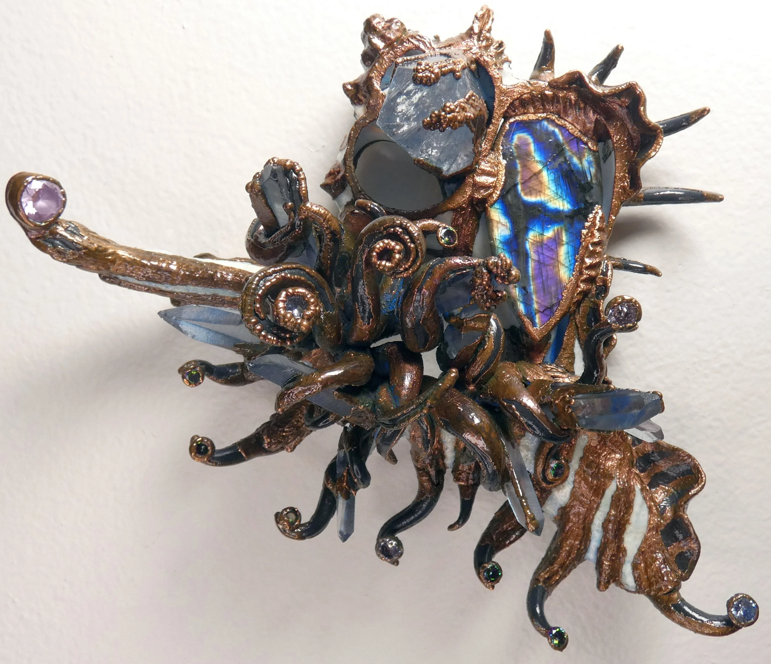 Emergence 002 (Through the Darkness): seashell slice, spectrolite, faceted lab alexandrite, quartz crystals, rhinestones, epoxy clay, electroformed copper. 6" H x 7" W x 3" D wall sculpture with keyhole slot. Available $1000.