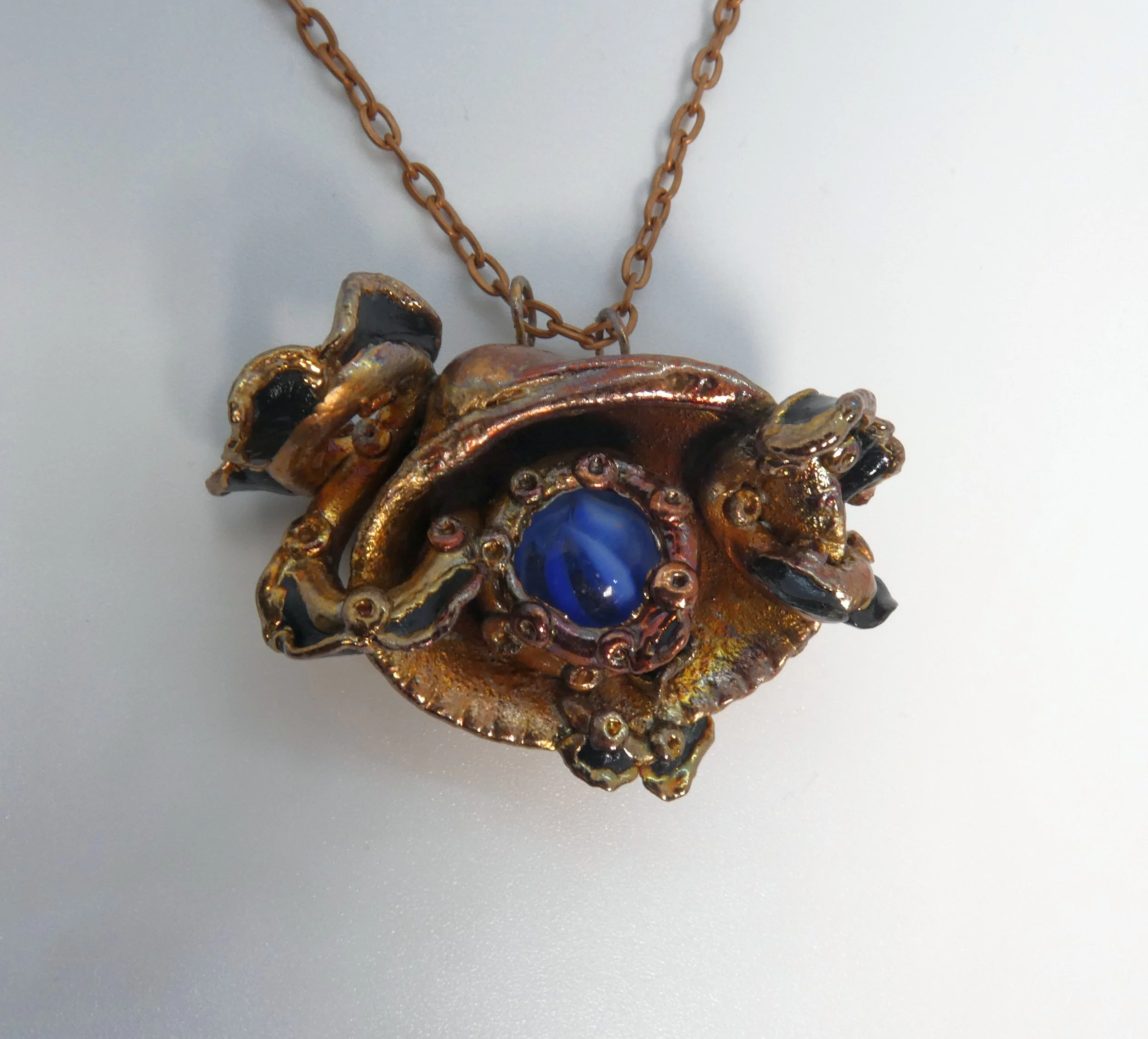 Symbiont 004 (Pendant): seashell with moving vintage blue cat’s eye marble held in epoxy clay tentacles and frills, electroformed in copper. 2” H x 2.5” W. In private collection.