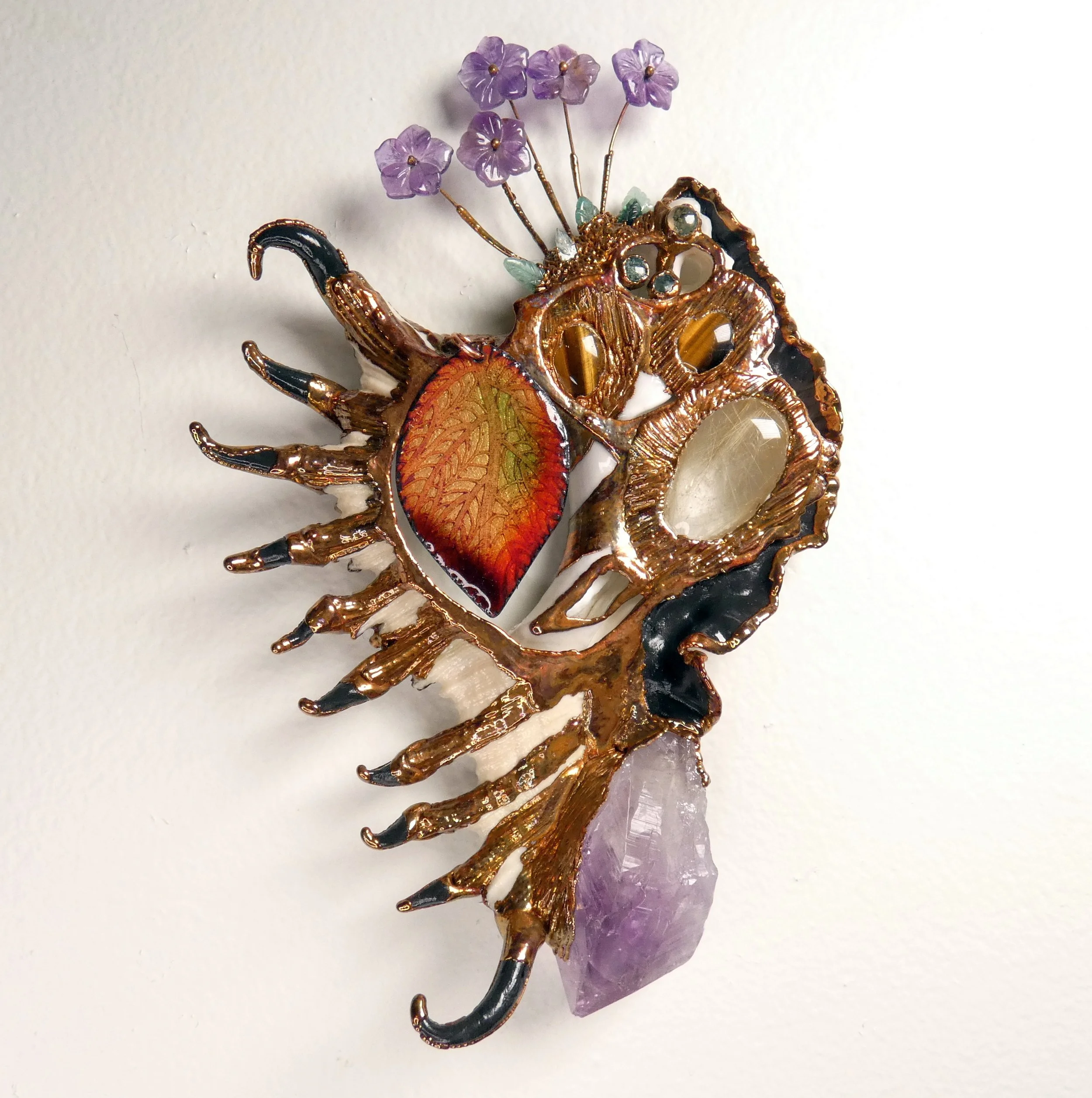 Symbiont 050 (Wall sculpture): enameled etched copper, seashell slice, amethyst point, rutilated quartz, tiger eye, moss agate, carved emerald leaves and amethyst flowers, copper headpins, epoxy clay, electroformed copper. 8" H x 5" W x 2” D. In priv