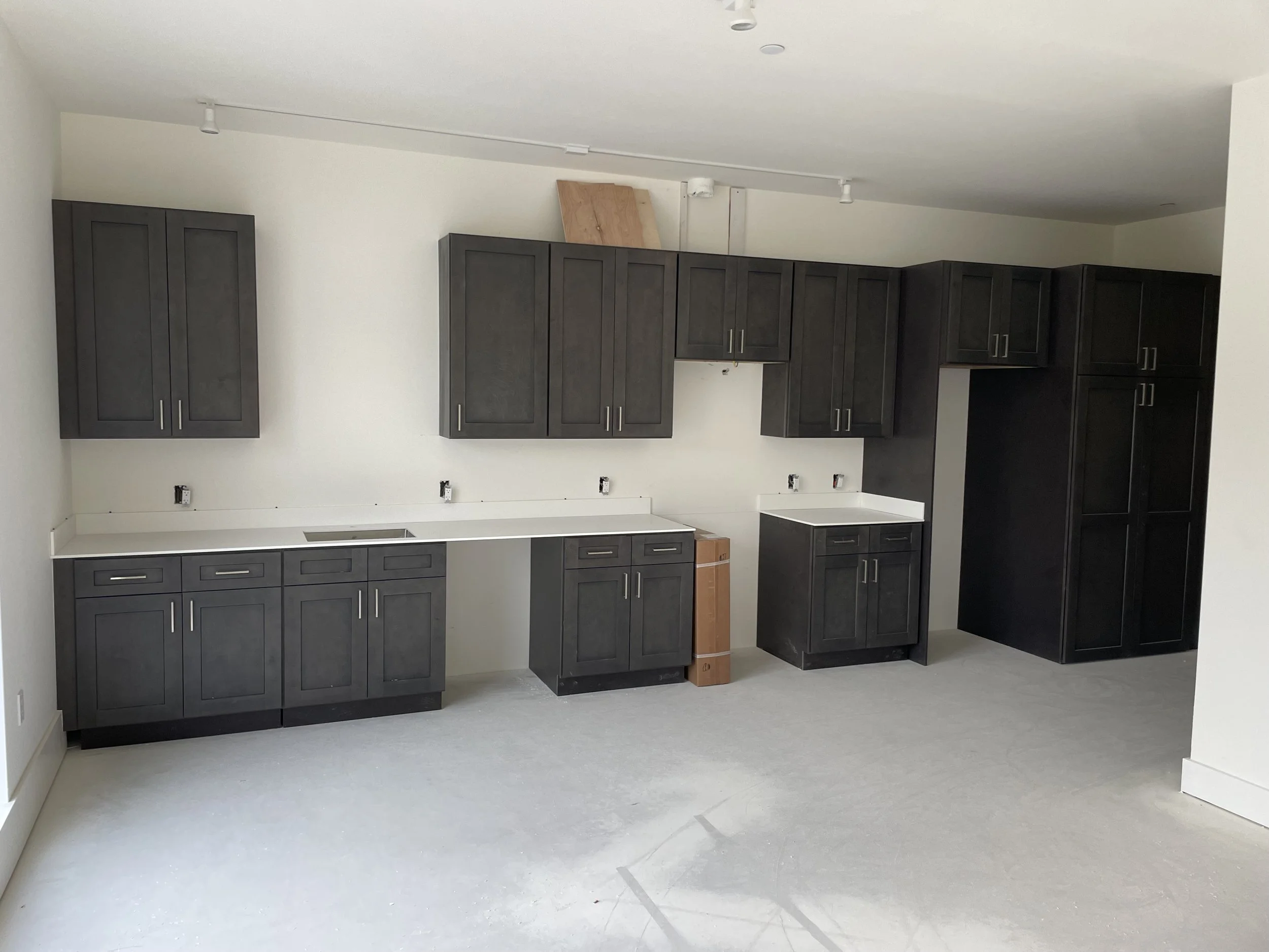Kitchen with black cabinets and white countertops, unfinished with electrical outlets and no appliances installed.
