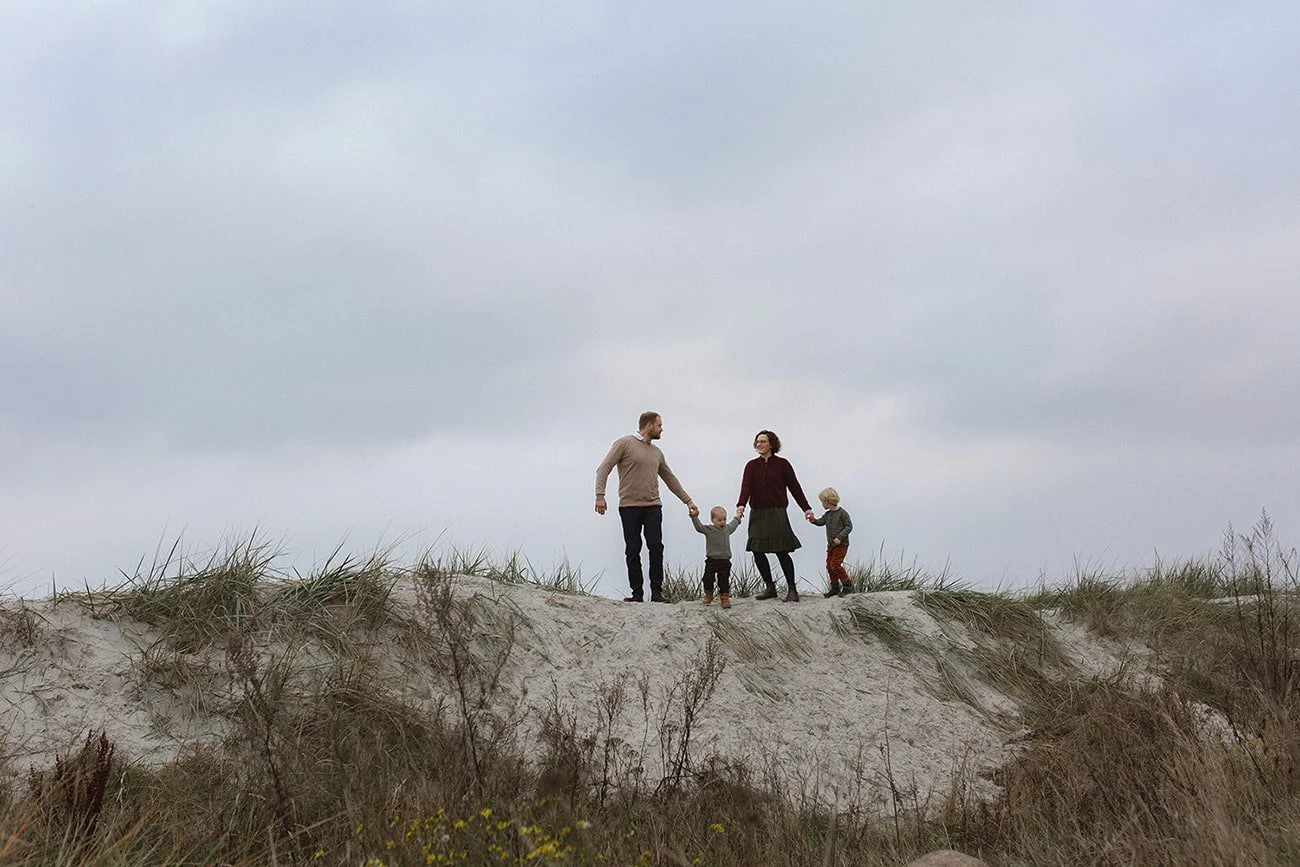 Familj med två barn går tillsammans över sanddynerna vid stranden i Lomma under en mycket mulen eftermiddag.