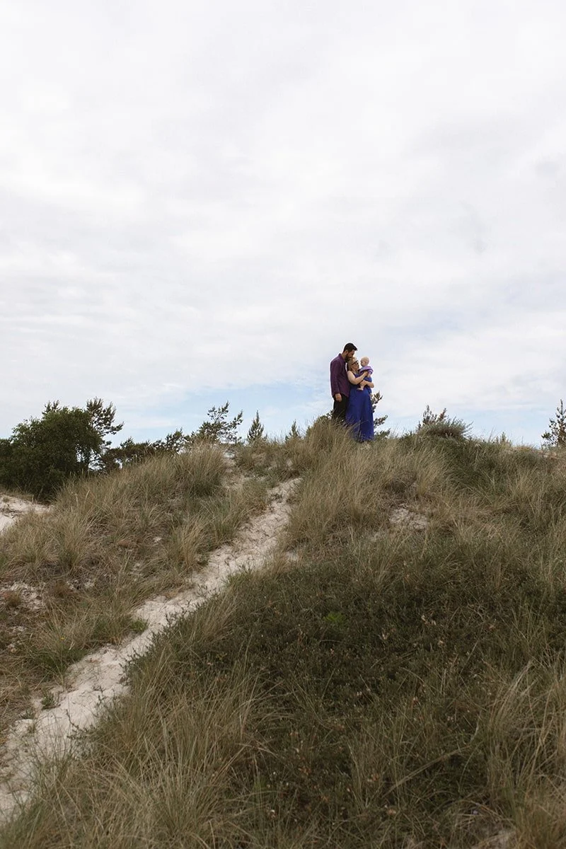 Familj med bebis promenerar genom sanddynerna vid havet i Falsterbo en mulen morgon i juni.