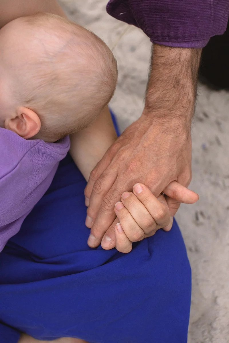 Närbild av en bebis och en förälders händer under en familjefotografering vid stranden i Falsterbo.