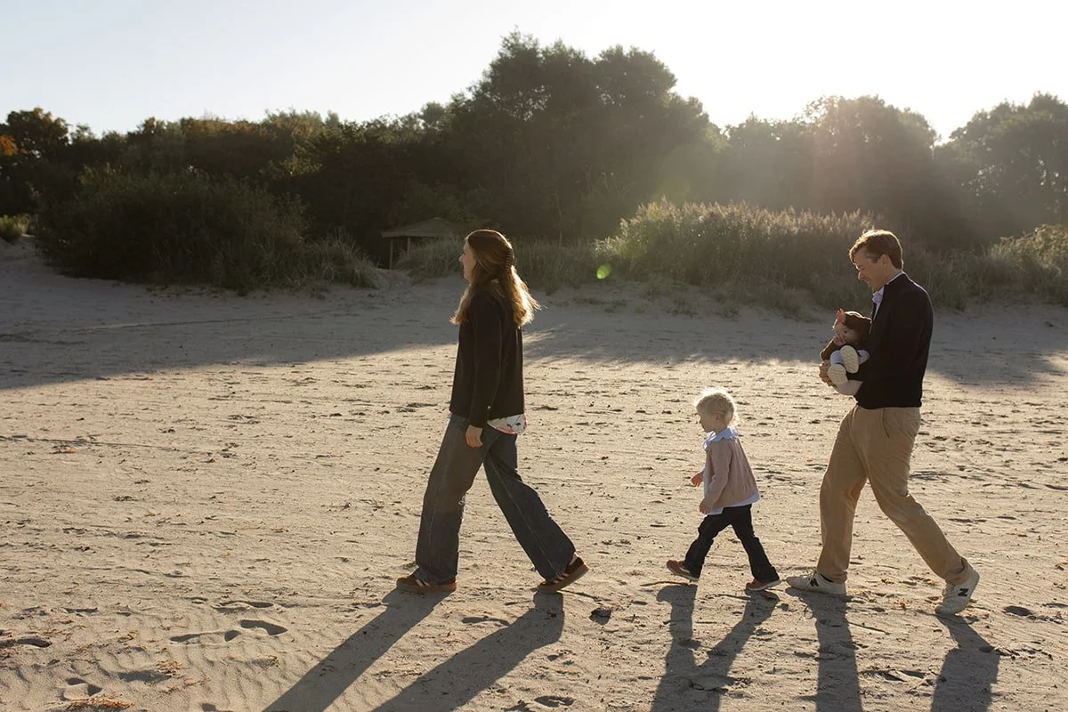 Familj promenerar tillsammans på stranden i Lomma i varmt eftermiddagsljus.