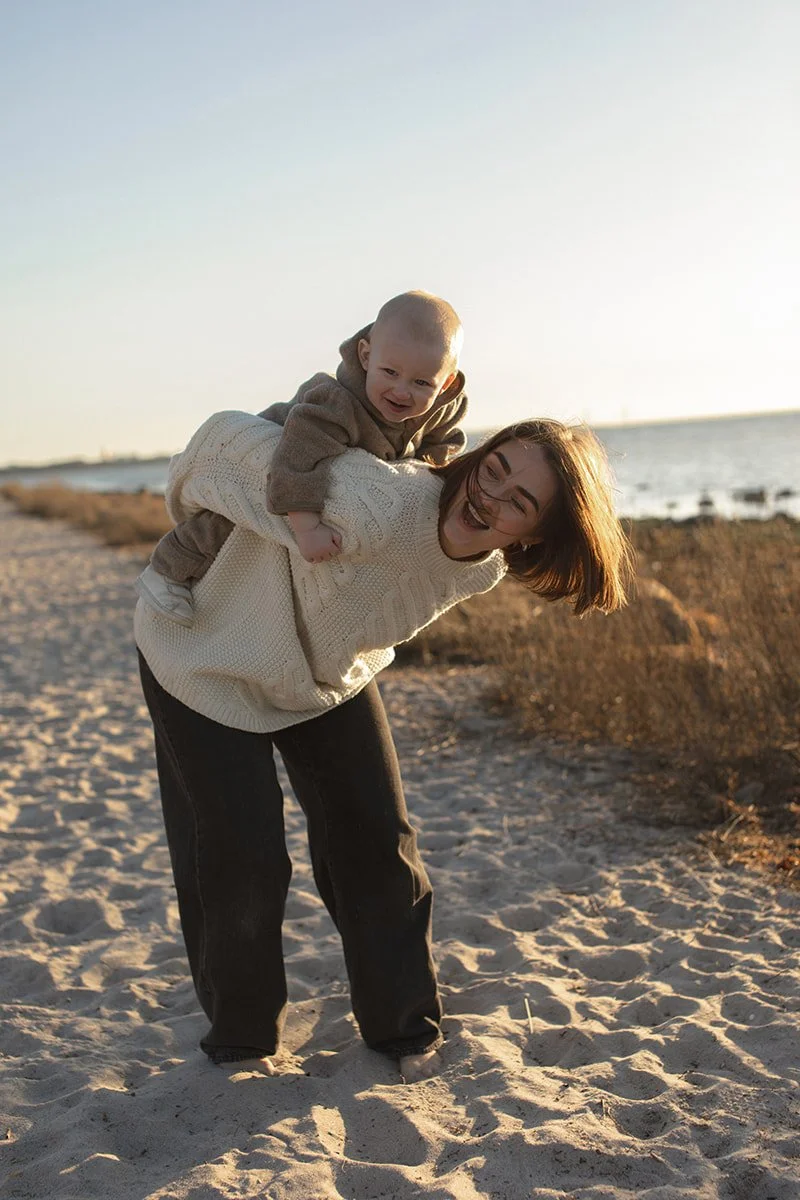 Mamma håller sitt barn på stranden i Lomma i varmt eftermiddagsljus.