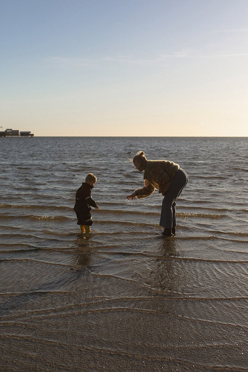 Mamma och barn leker i havet vid stranden i Bjärred i varmt eftermiddagsljus.