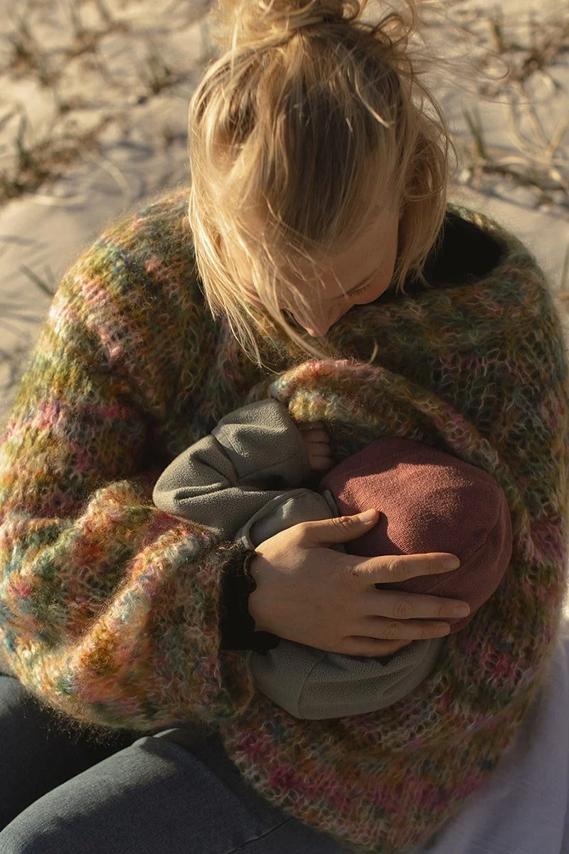 Barn sitter nära sin förälder med en bebis vid stranden i Bjärred i varmt vårsolljus.