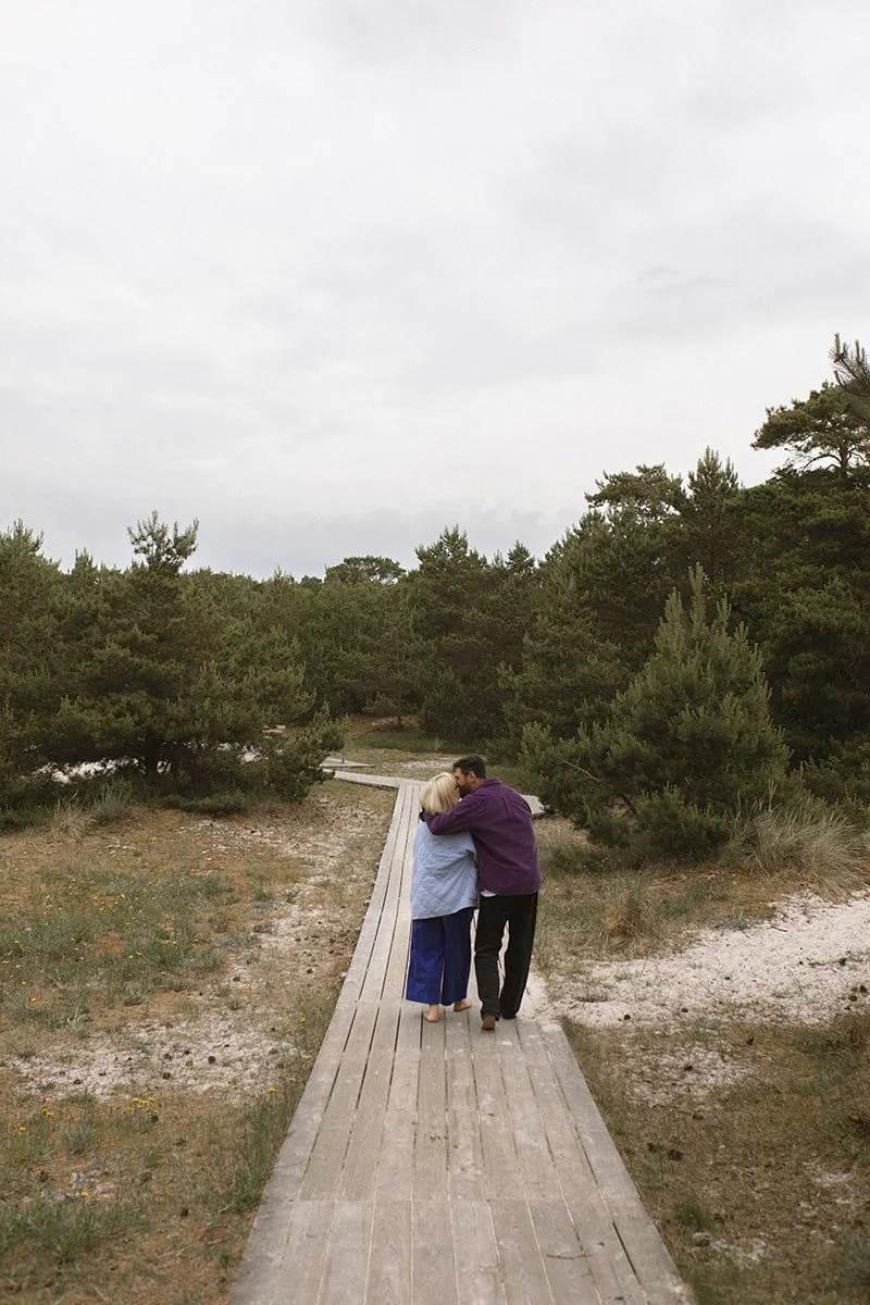 Föräldrar promenerar tillsammans på en träspång vid havet i Falsterbo en solig morgon i juni.