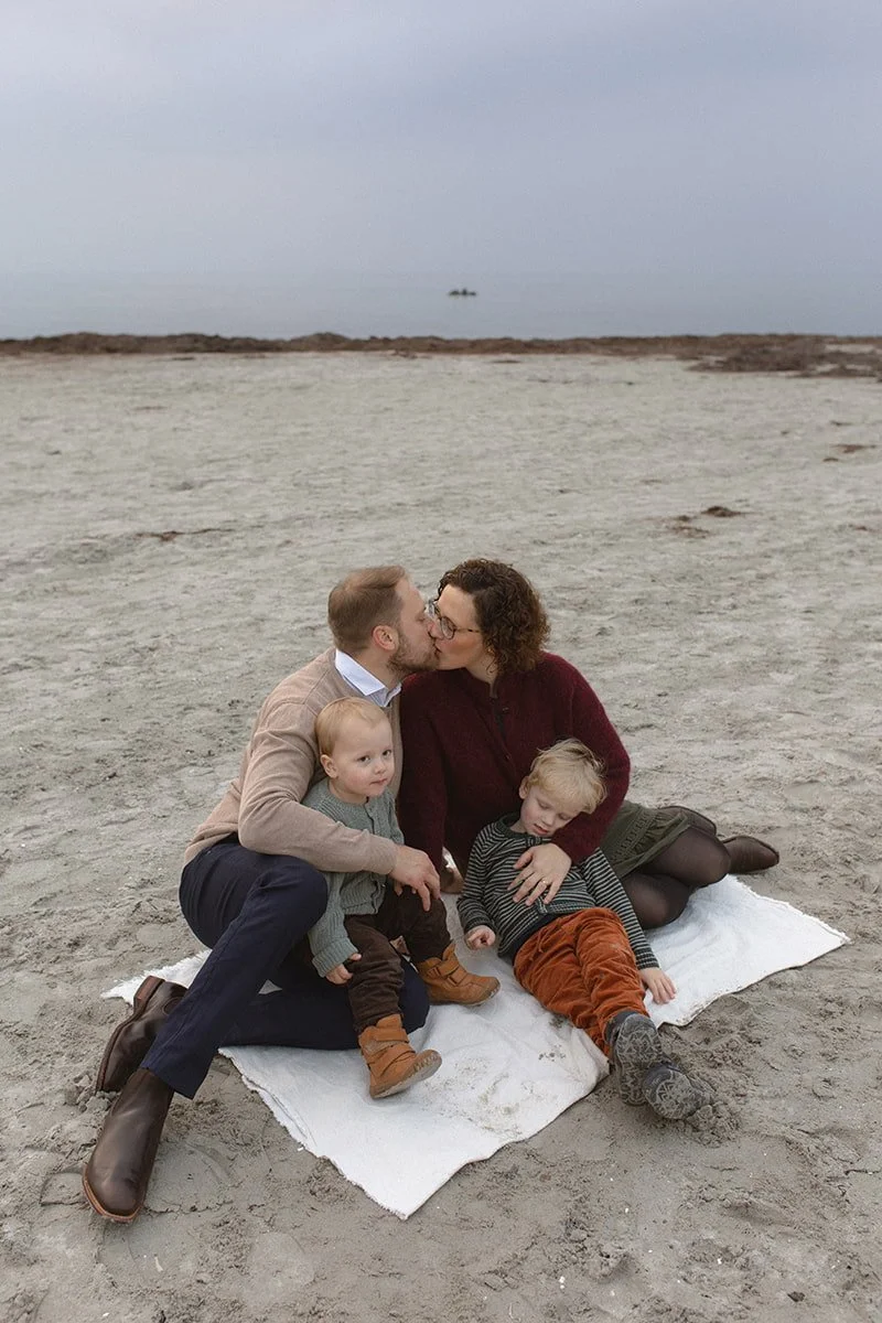 Familj med två barn sitter på en filt på stranden i Lomma under en mulen eftermiddag i november.
