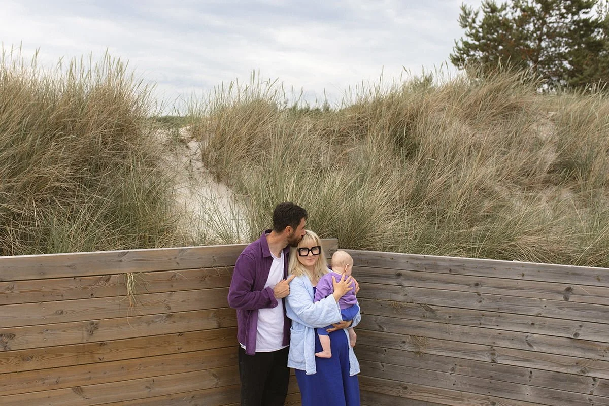 Familjefotografering vid stranden i Falsterbo med föräldrar och bebis en mulen morgon i juni.