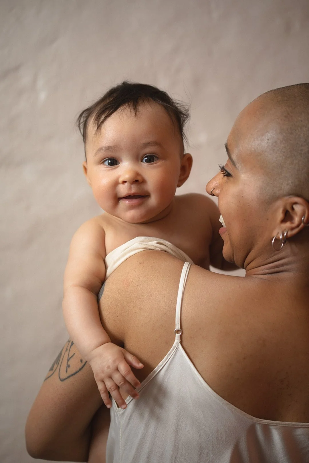 Smiling baby held by mother during a natural motherhood photography session in Malmö. Warm family portrait capturing joyful everyday moments.