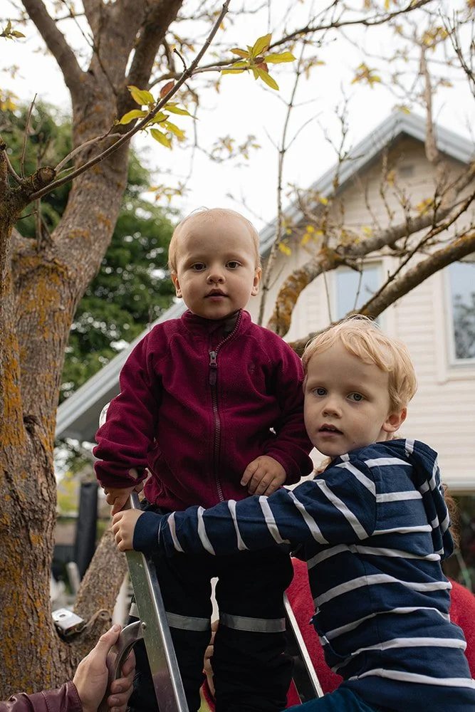 Syskon sitter tillsammans i trädgården under familjefotografering hemma, naturliga barnbilder i Lund