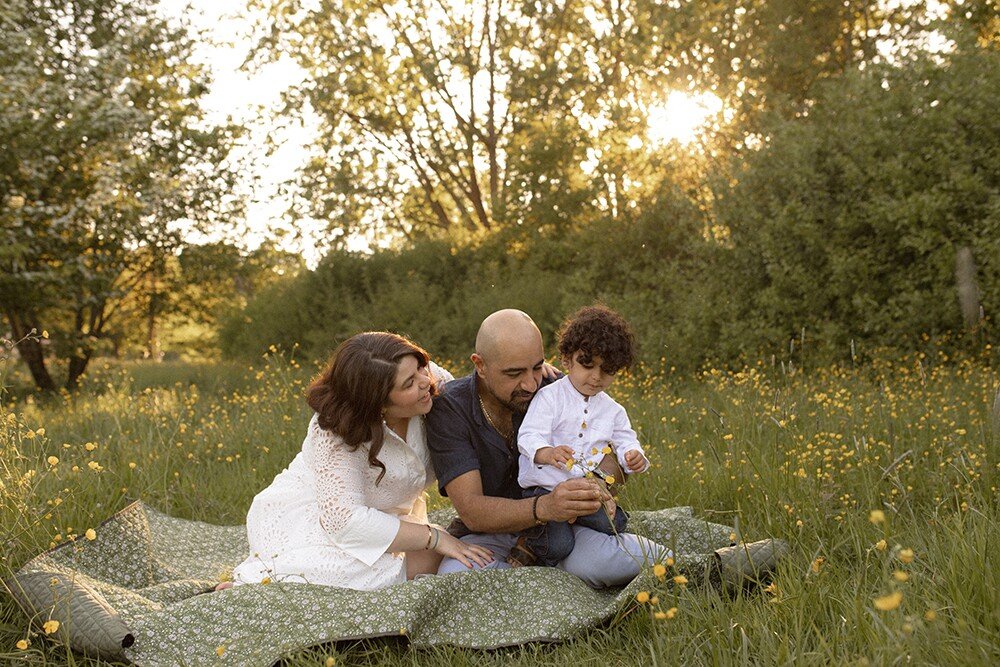 Familj sitter på filt på blommande äng i kvällsljus under vårfotografering