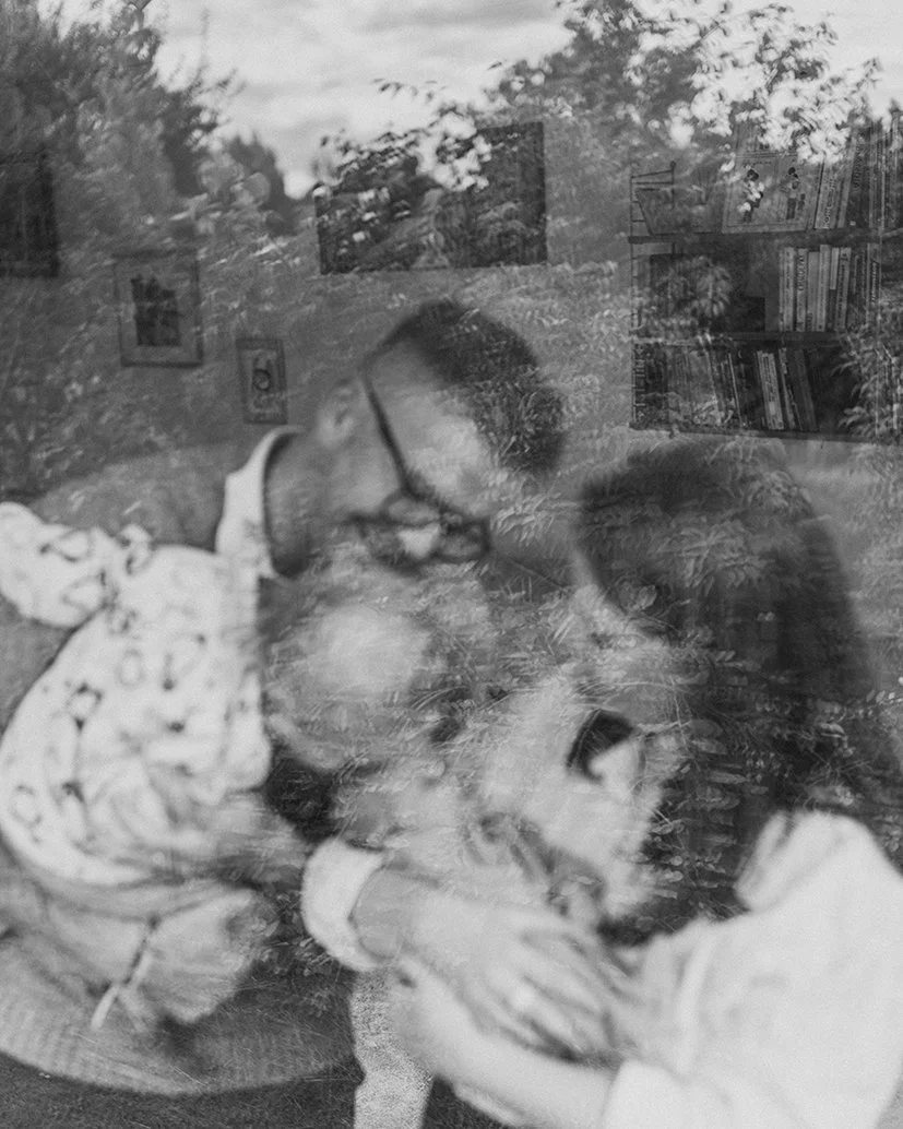 Konstnärlig bild genom ett fönster där naturen speglas i glaset, med en familj och deras nyfödda barn mjukt synliga i bakgrunden.