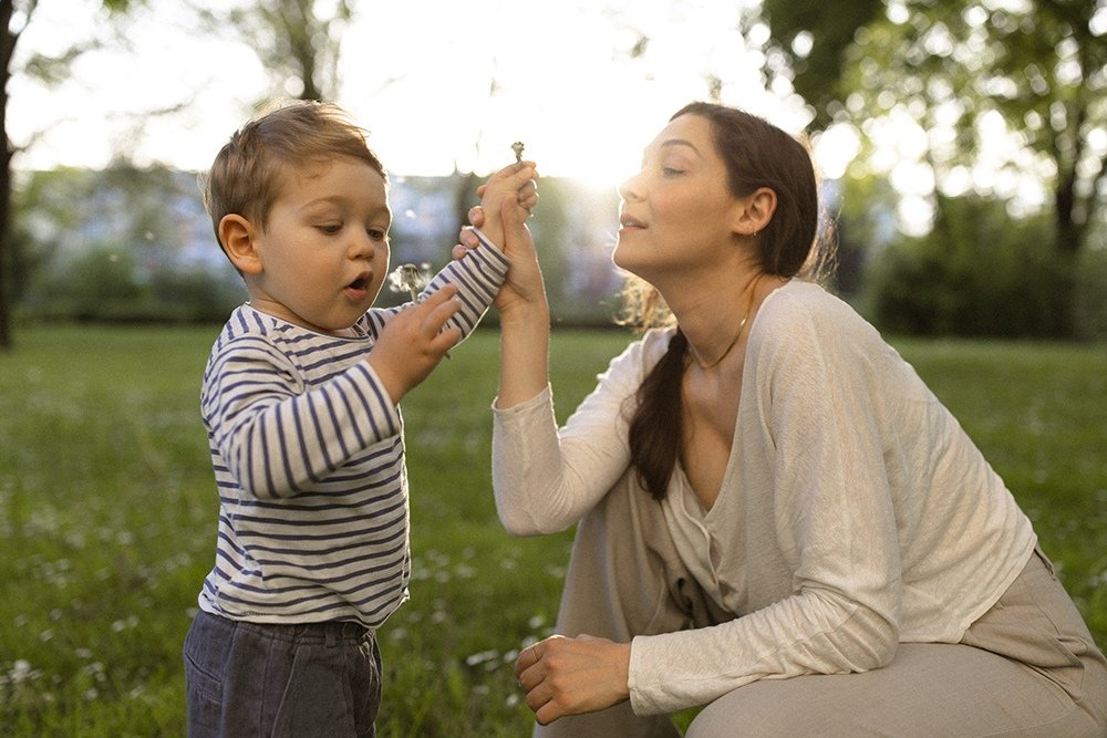 Mamma och son blåser maskrosor under lekfull familjefotografering på våren