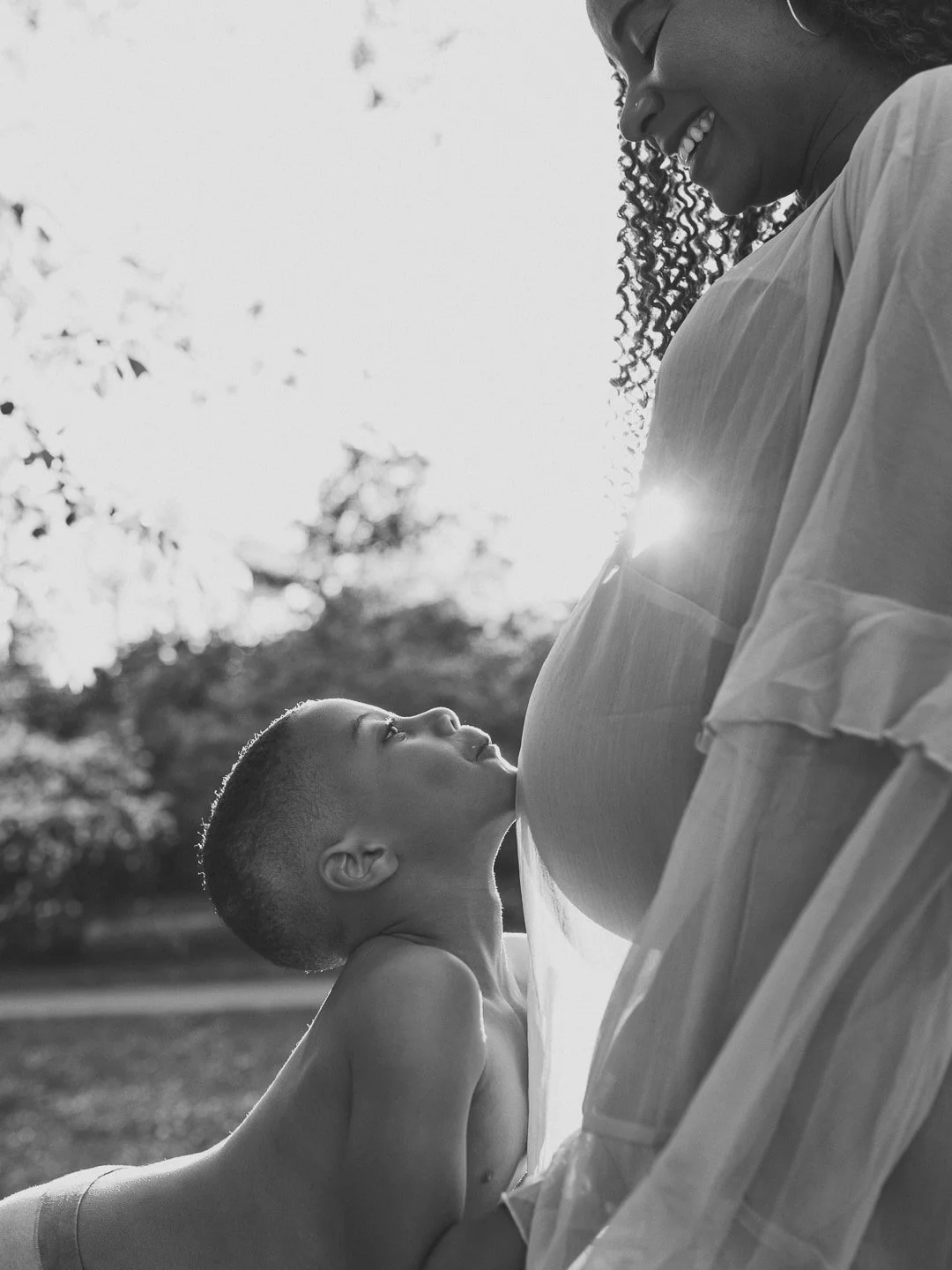 Litet barn lutar huvudet mot mammas gravida mage i mjukt kvällsljus