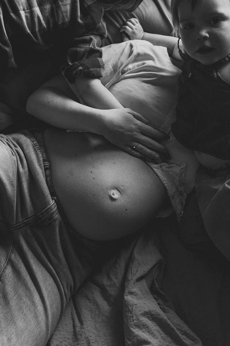 Naturlig gravidfotografering hemma i Lund där en blivande mamma och hennes barn delar en lugn stund tillsammans.