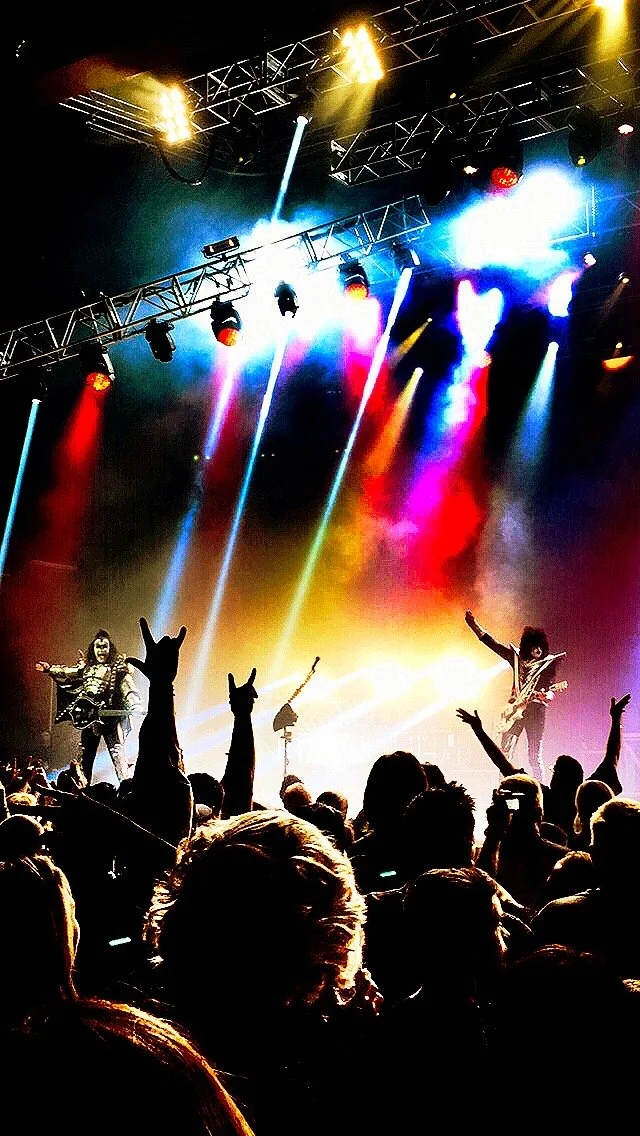 KISS concert. Rock concert stage with colorful lights and a band performing; audience with raised hands silhouettes.