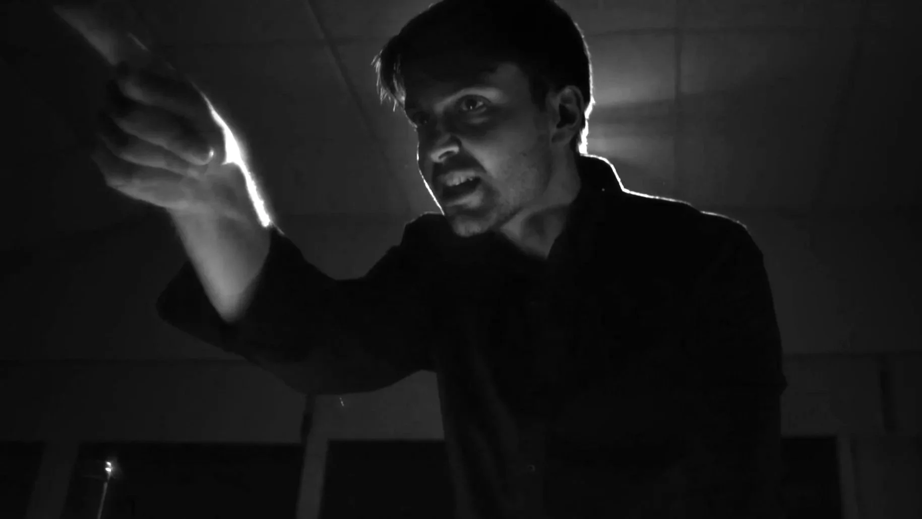 Pessoa com expressão de raiva ou raiva, segurando algo com força, em um ambiente escuro e com iluminação dramática.