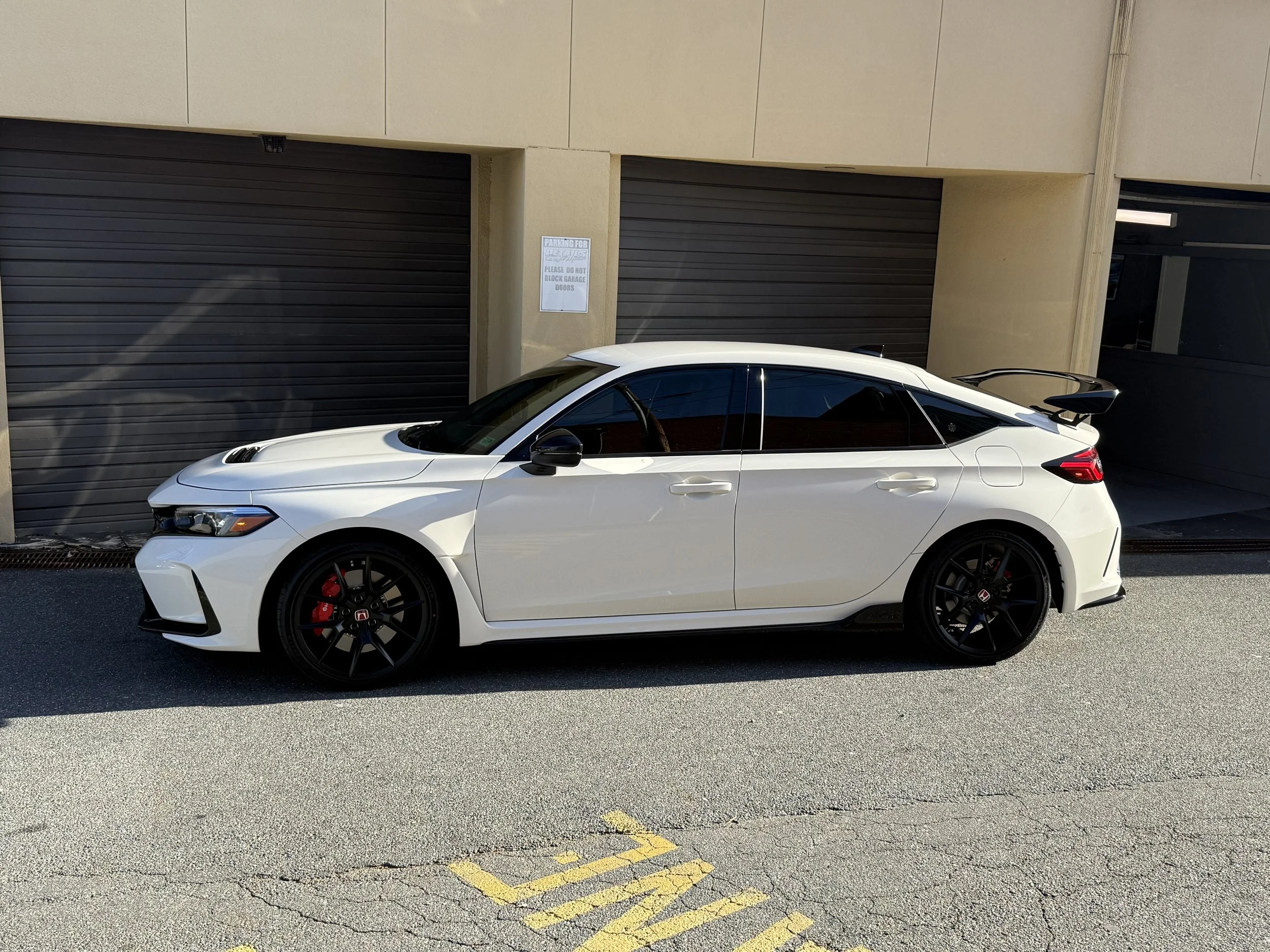 White sports car parked in front of a beige building with brown garage doors.