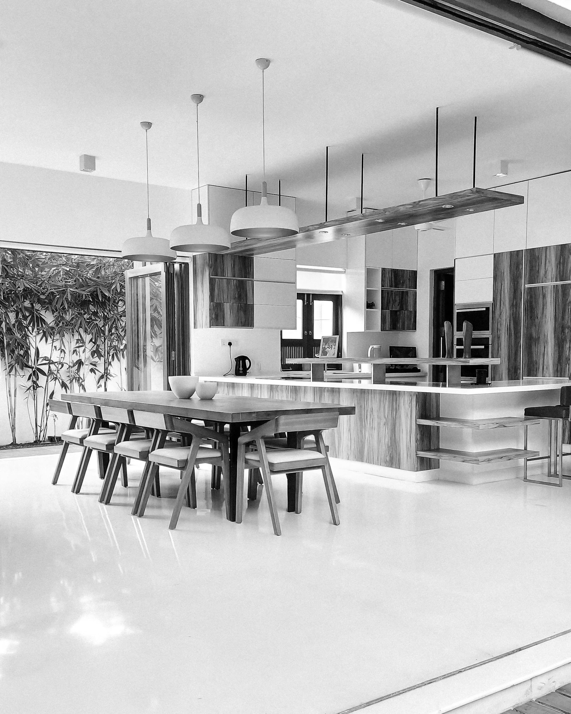 Modern kitchen and dining area with a wooden dining table, six chairs, pendant lighting, and a kitchen island with bar stools.