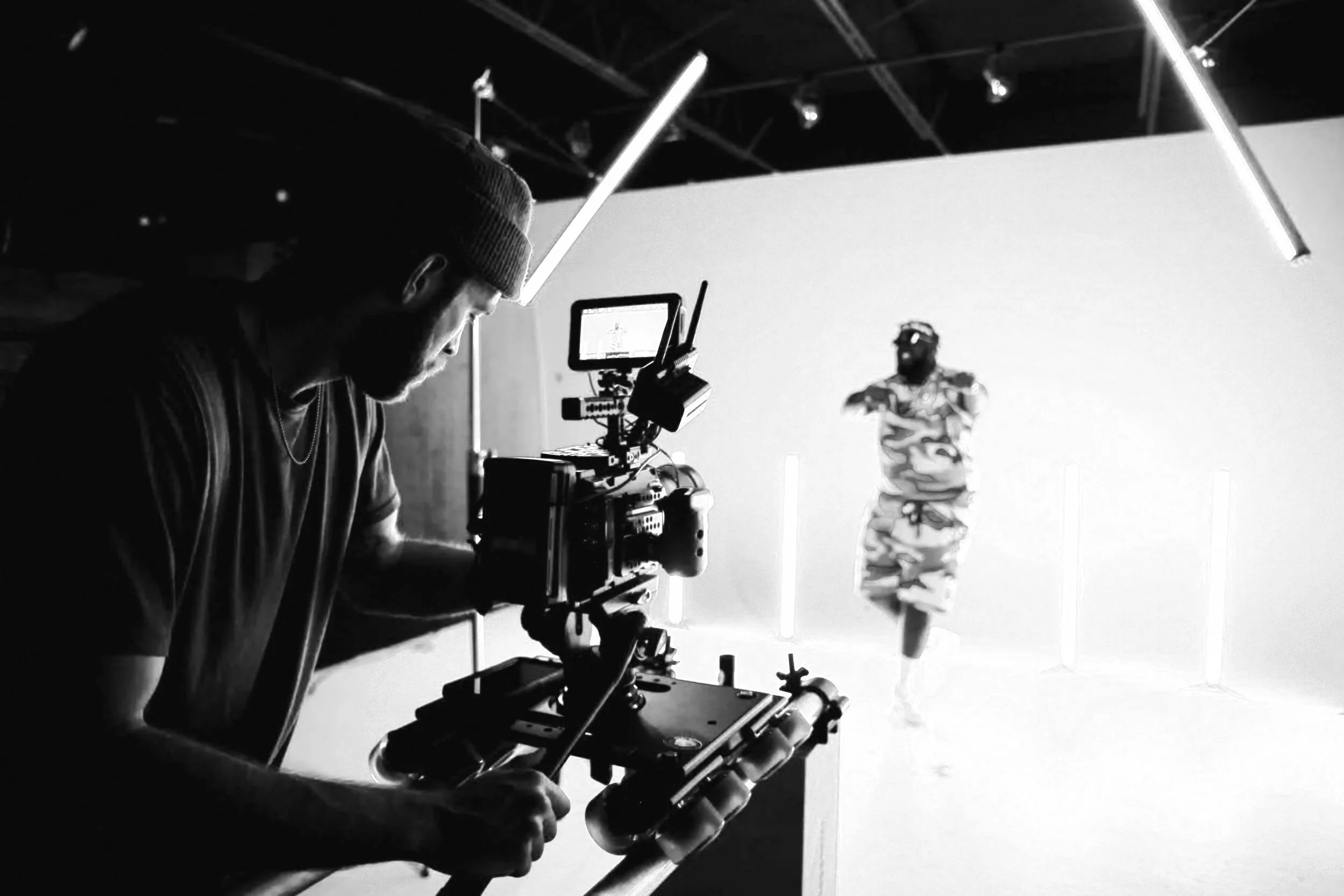 A videographer films a dancer in a studio with neon lights and a blue background.