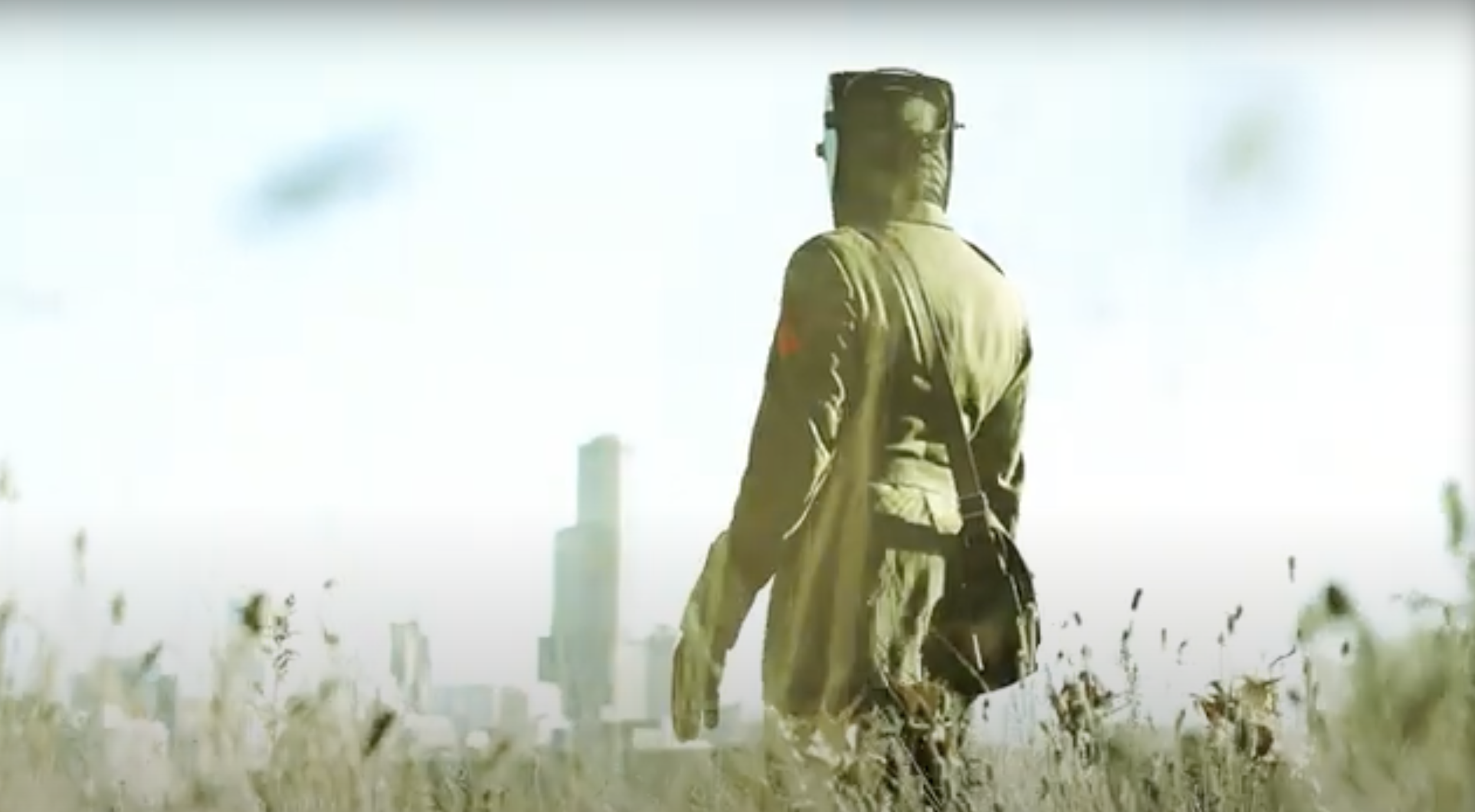 A person dressed in military gear, walking through tall grass in a cityscape with tall buildings in the background, under a bright sky.
