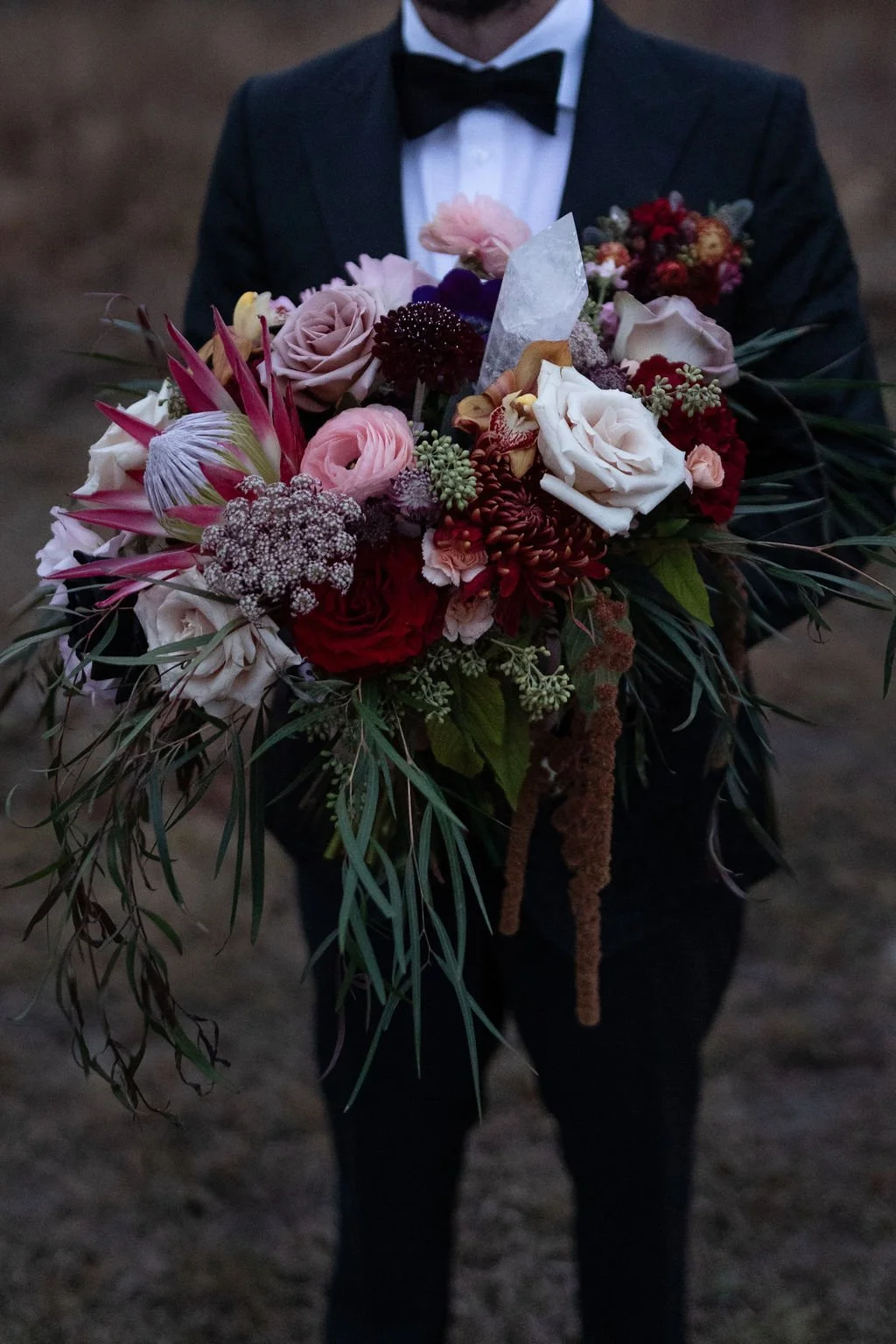 A man in a tuxedo holding a large, colorful bouquet of flowers.