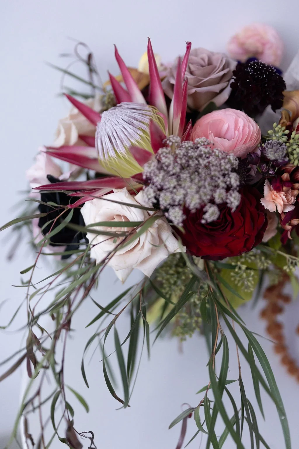Close-up of a colorful bouquet with pink, red, white, and purple flowers, including roses, protea, and various greenery.