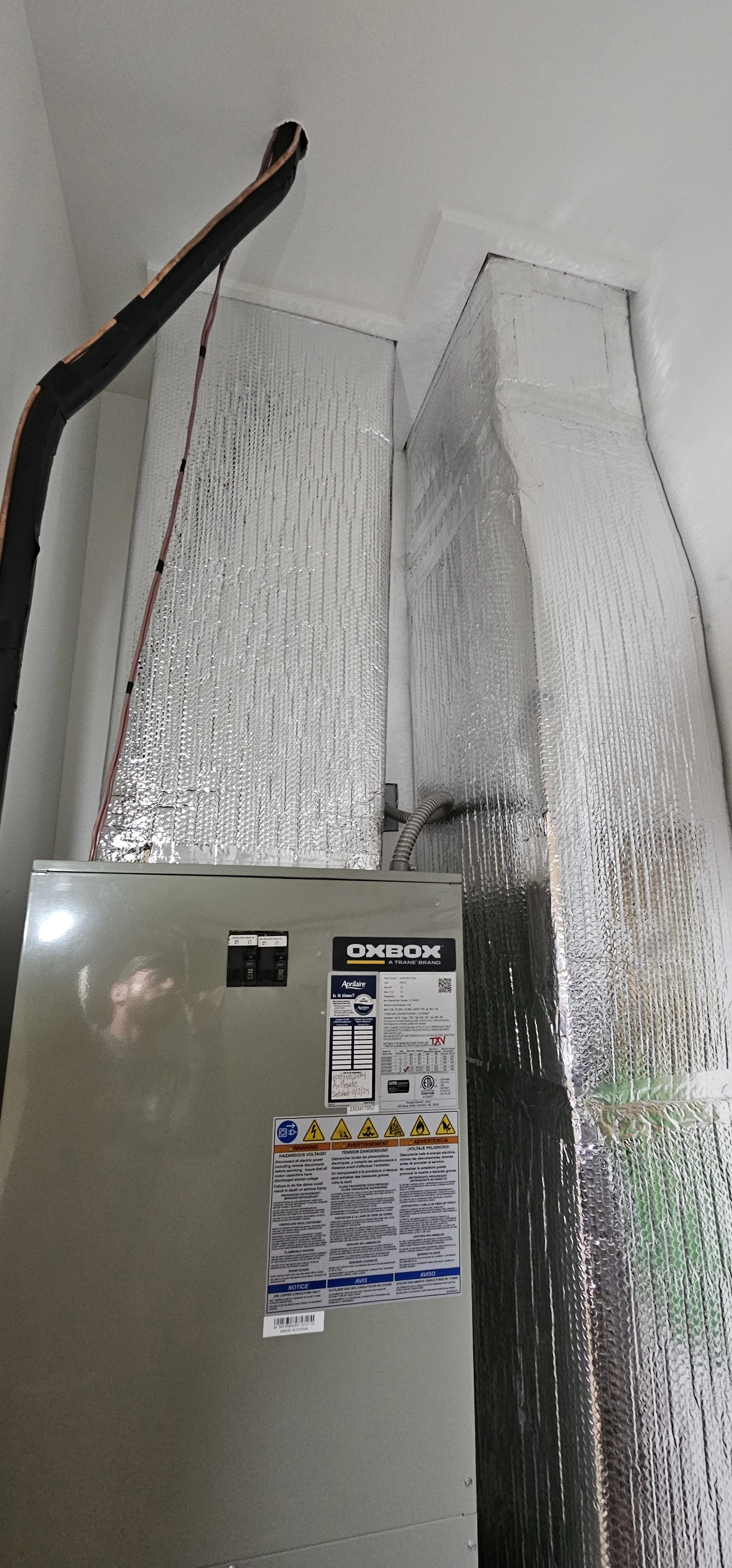 The image shows a heating or air conditioning unit with reflective insulation ducting installed around it. The unit has a label with the brand name OXBOX.