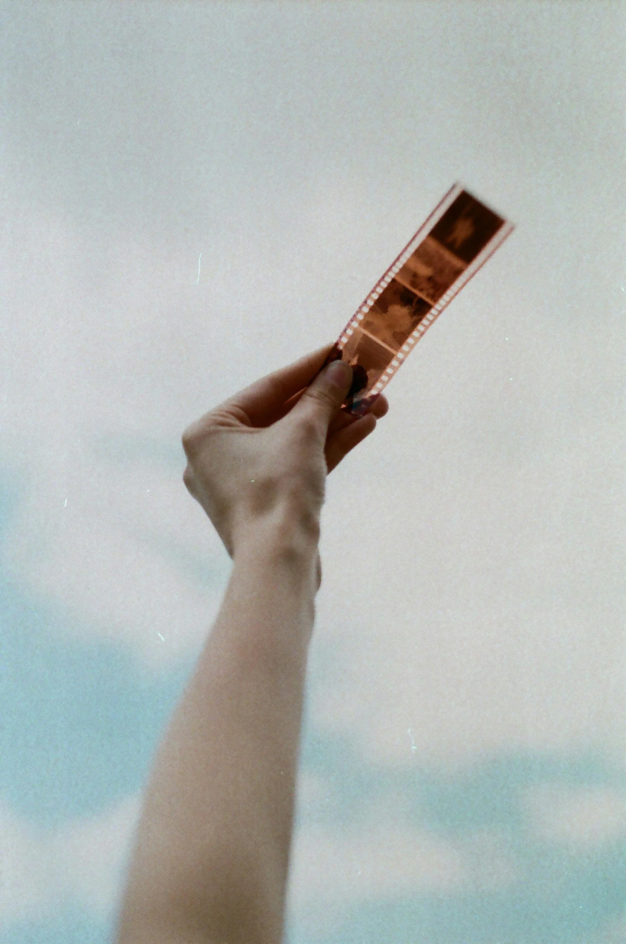 A person holding a strip of film up against a light-colored ceiling.