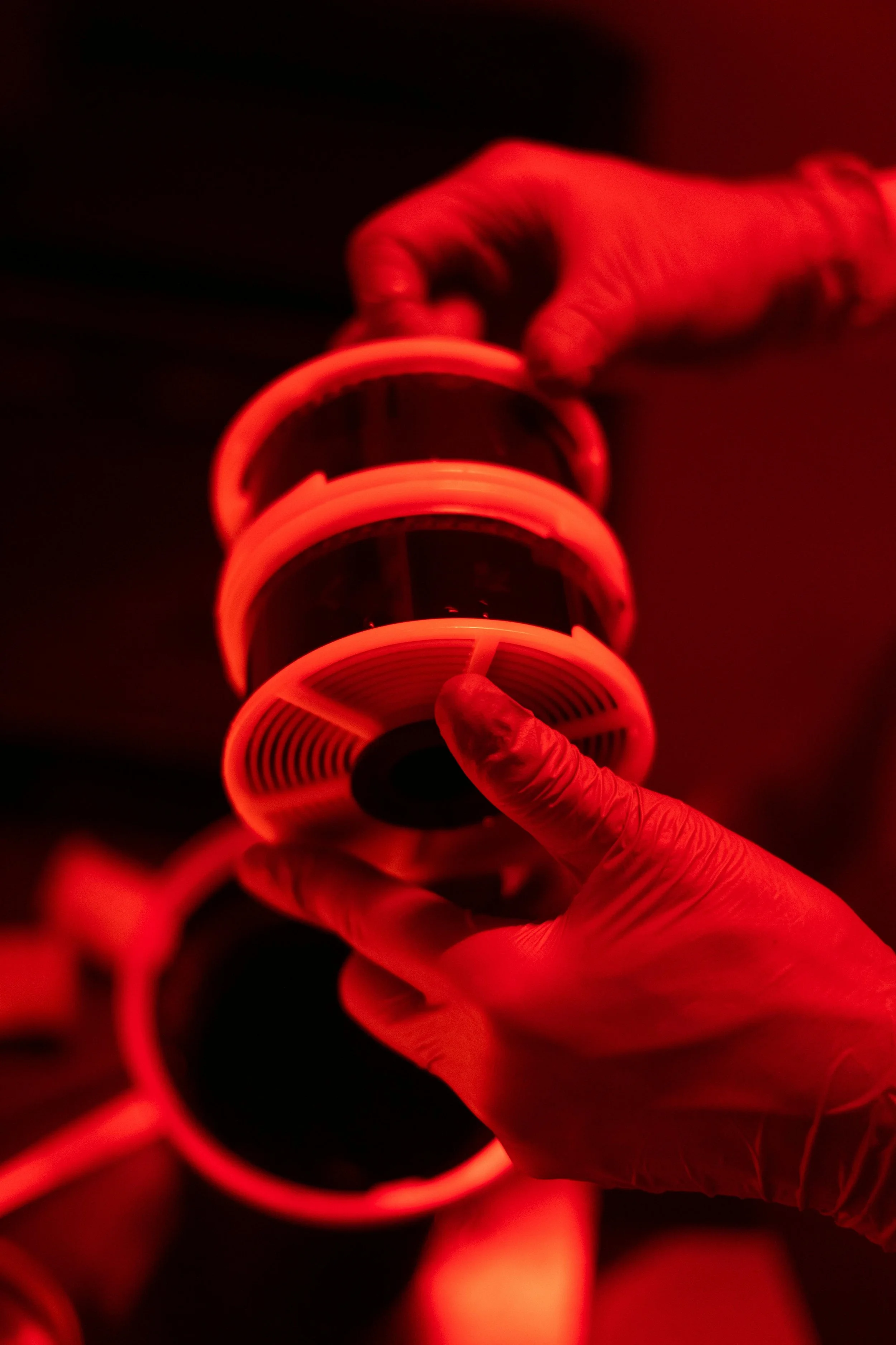 Close-up of a person wearing gloves holding a stack of black and white film reels, illuminated by red lighting.