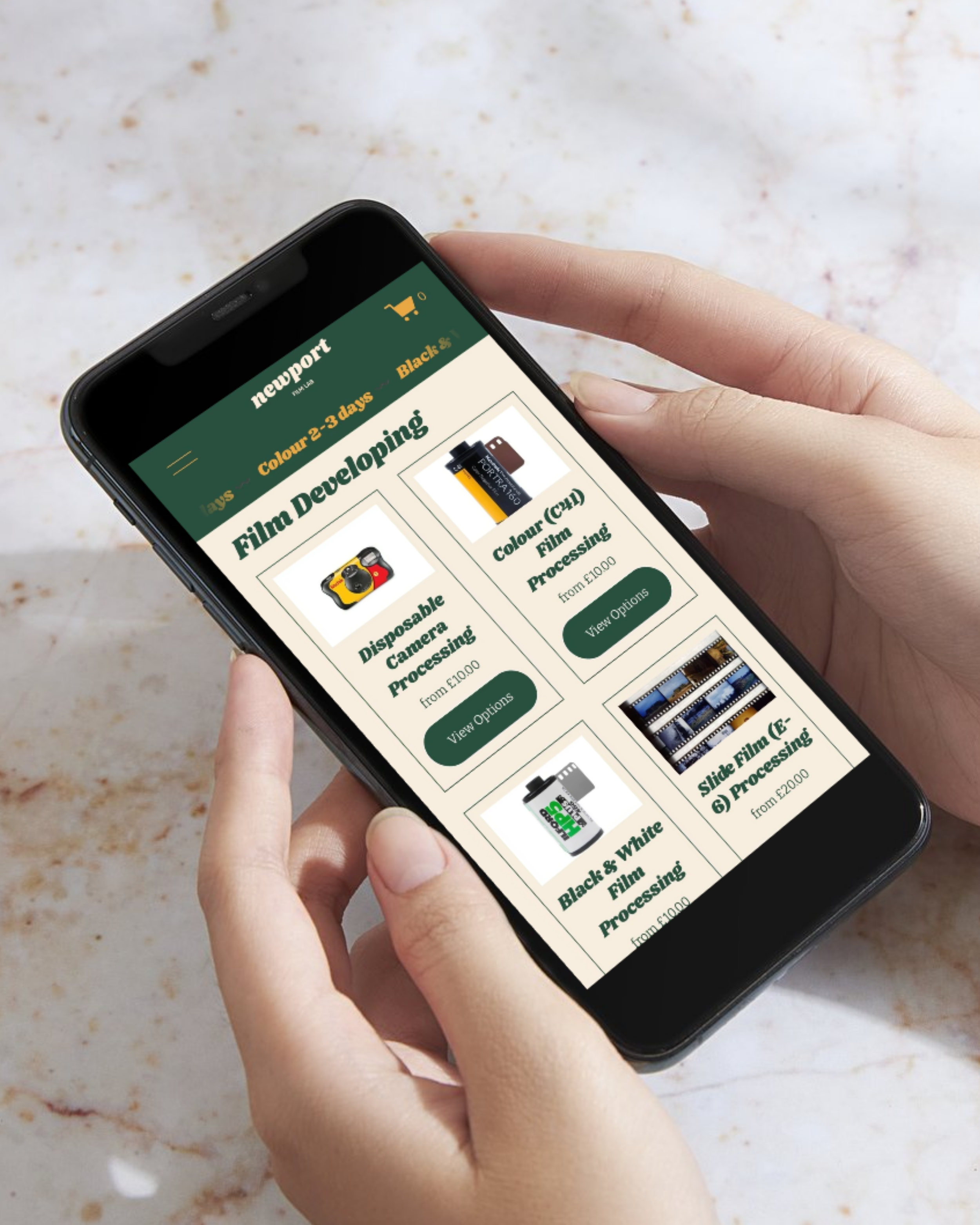 Person holding a smartphone displaying an online film developing store with options for various film processing services, including disposable camera, black and white, color, and slide film processing, with prices listed.