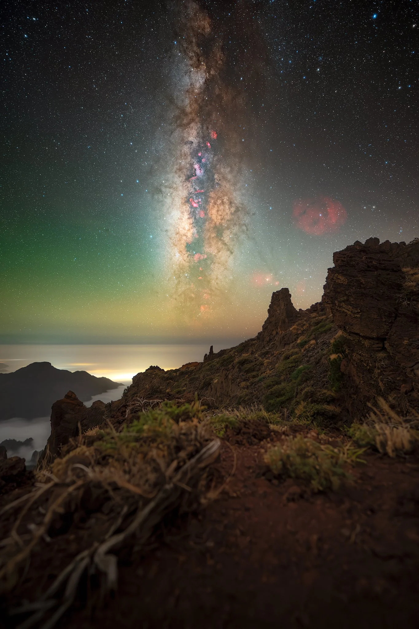 A night view of the Milky Way galaxy above a rugged mountain landscape with clouds in the distance.