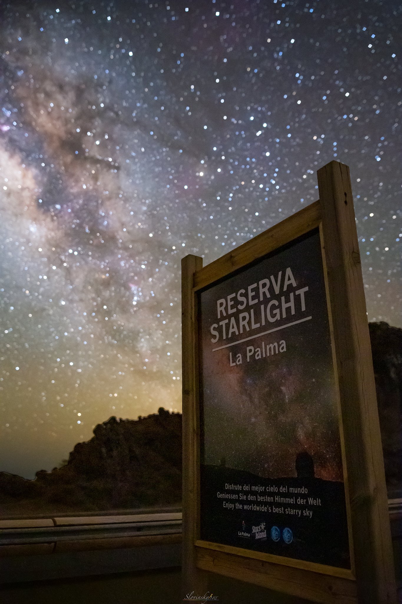 Night sky filled with stars and the Milky Way galaxy, with a sign that reads 'Reserva Starlight La Palma' in the foreground.