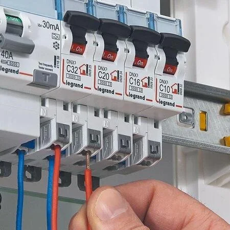 Un tableau électrique avec des disjoncteurs Schneider Electric, câbles rouges, bleus et gris connectés à chaque disjoncteur.