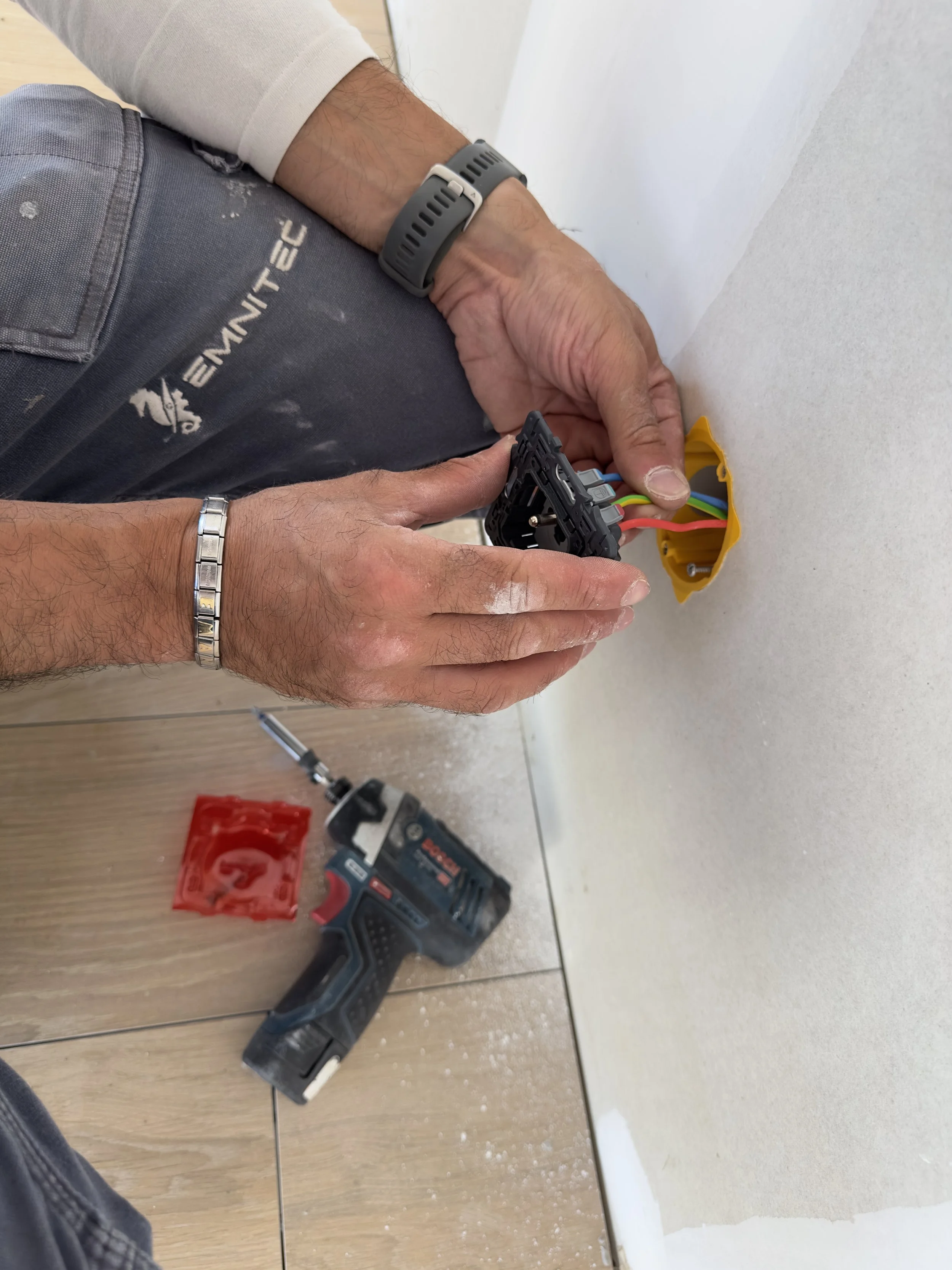 Une personne utilise un tournevis pour fixer une prise électrique murale blanche avec deux emplacements pour des fiches, contre un mur blanc