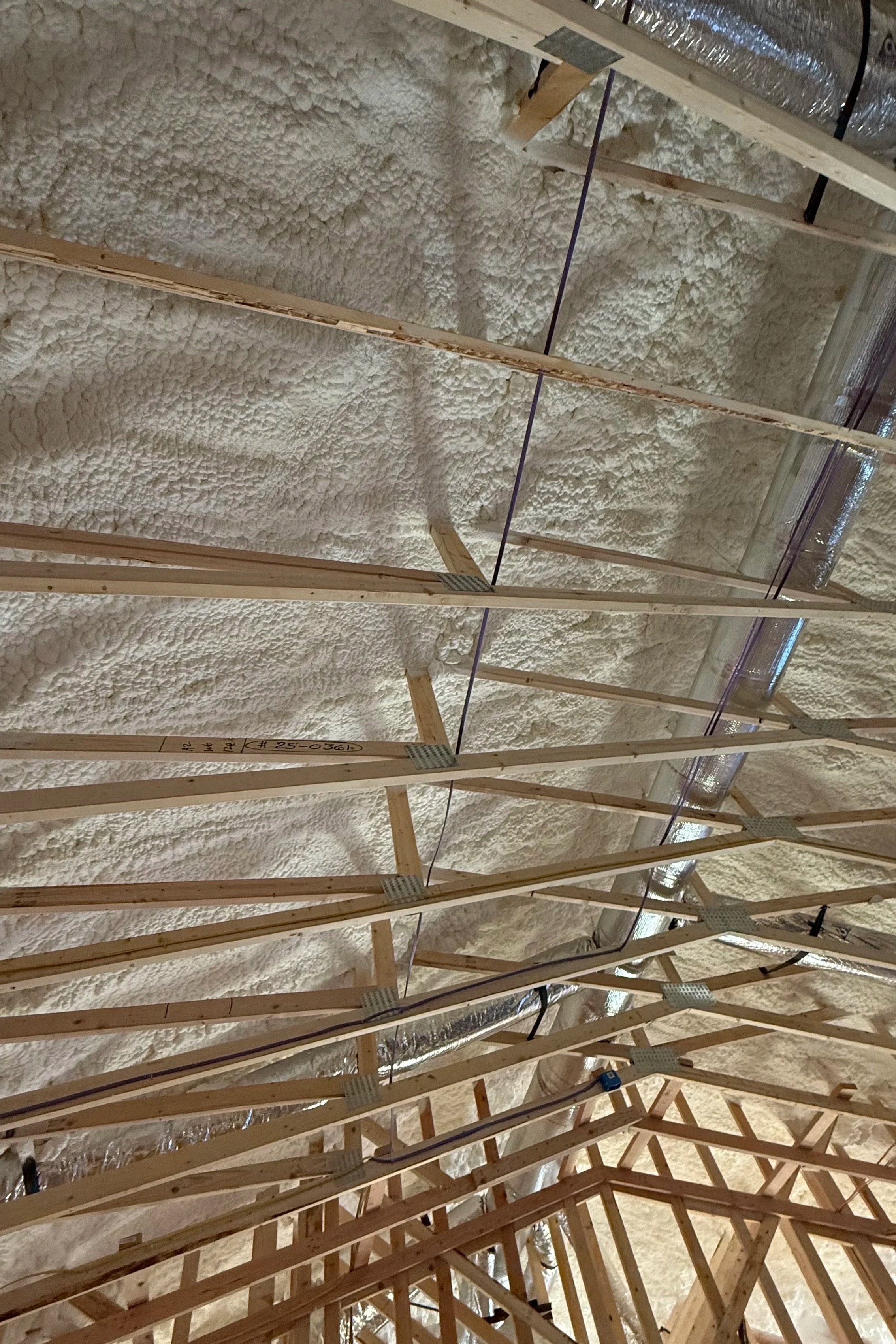 View of a ceiling under construction showing wooden framework, insulation foam, and HVAC ductwork.
