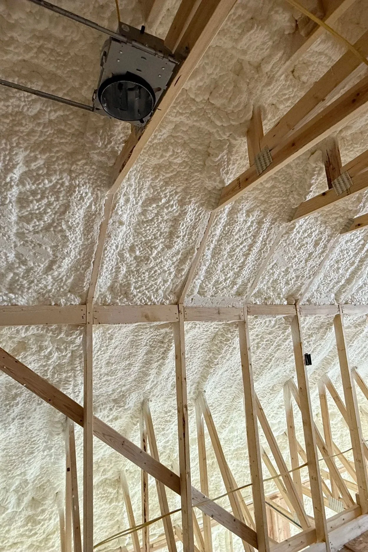 Interior view of a building under construction, showing wooden framing and spray foam insulation on the roof.