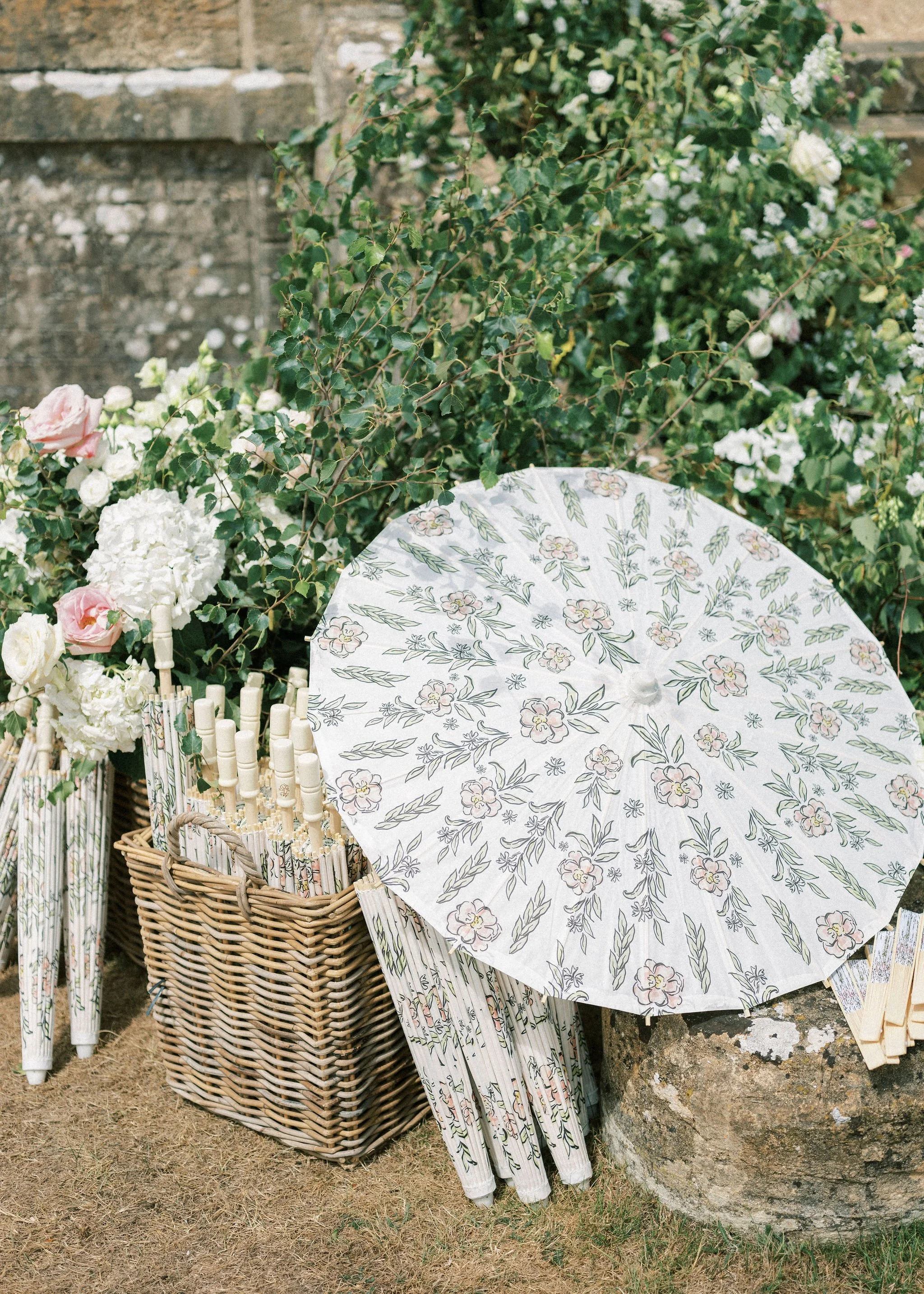 An image showing custom paper parasols for a wedding arranged in a basket, using designs from the wedding stationery on the parasols