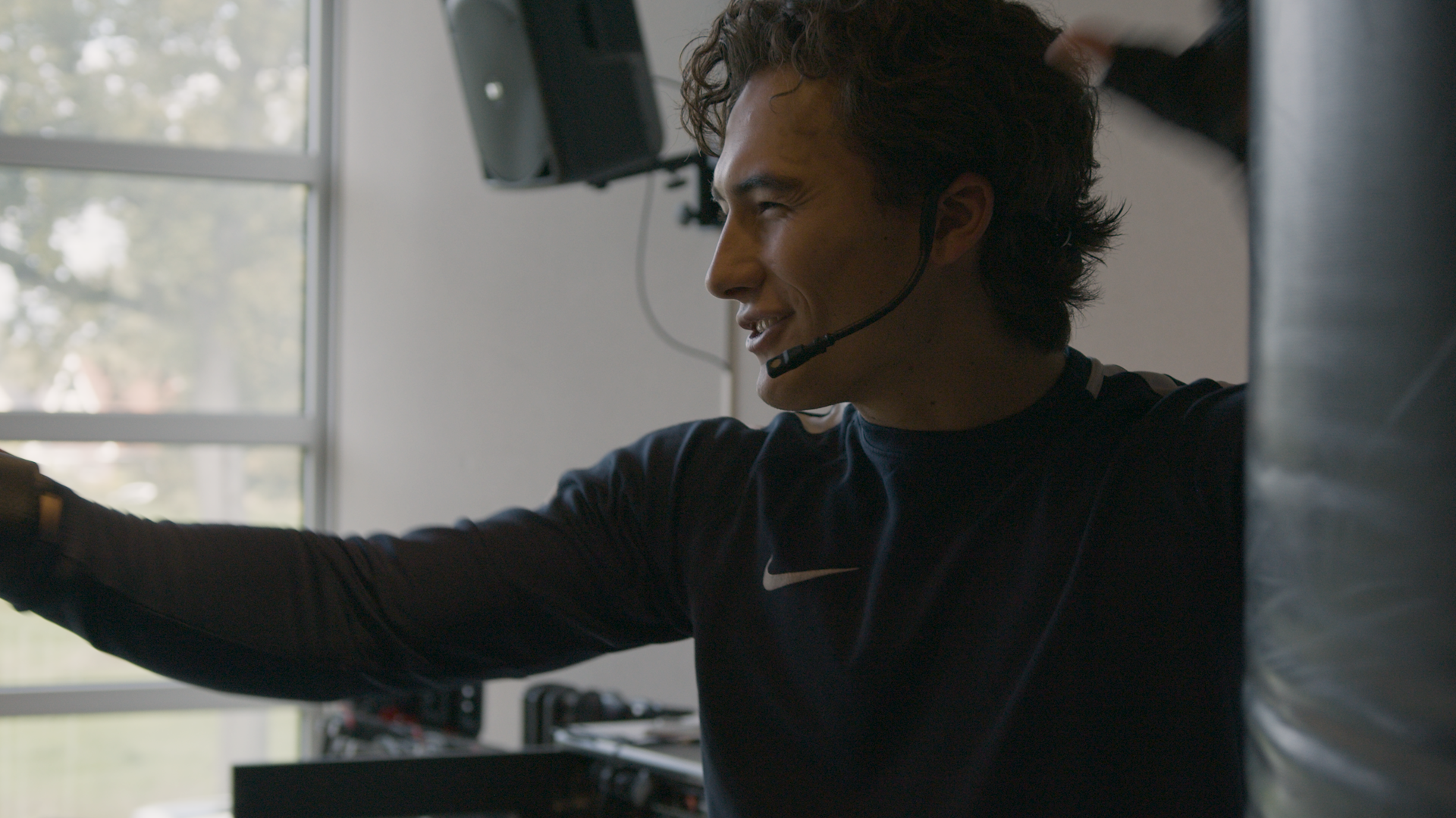 Moderne houten gebouw met grote glazen raam, gelegen in een bergachtig landschap met gele struiken en bergen op de achtergrond.