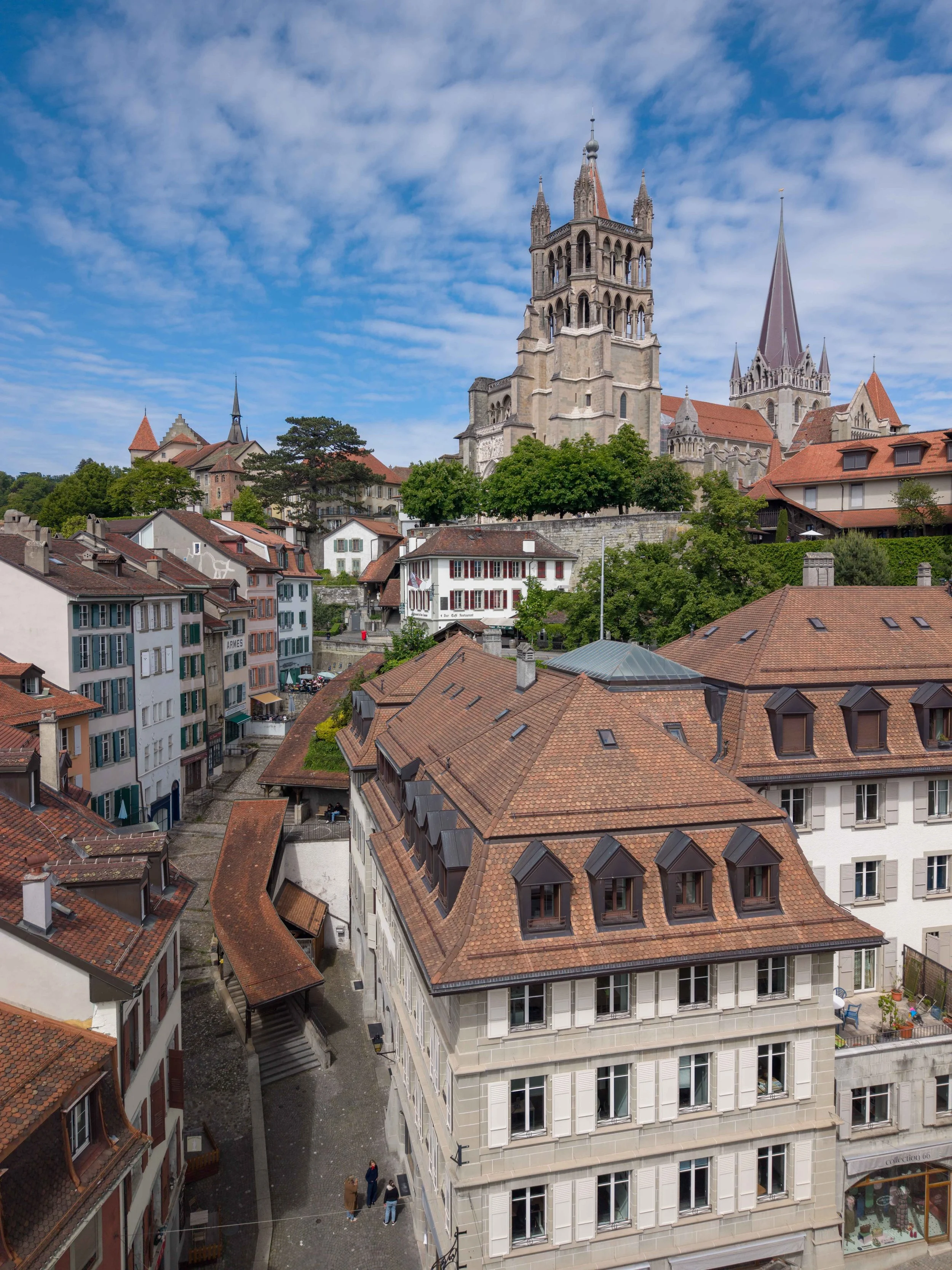Ville avec bâtiments anciens et église avec grande tour et toiture en ardoise, ciel bleu avec quelques nuages.
