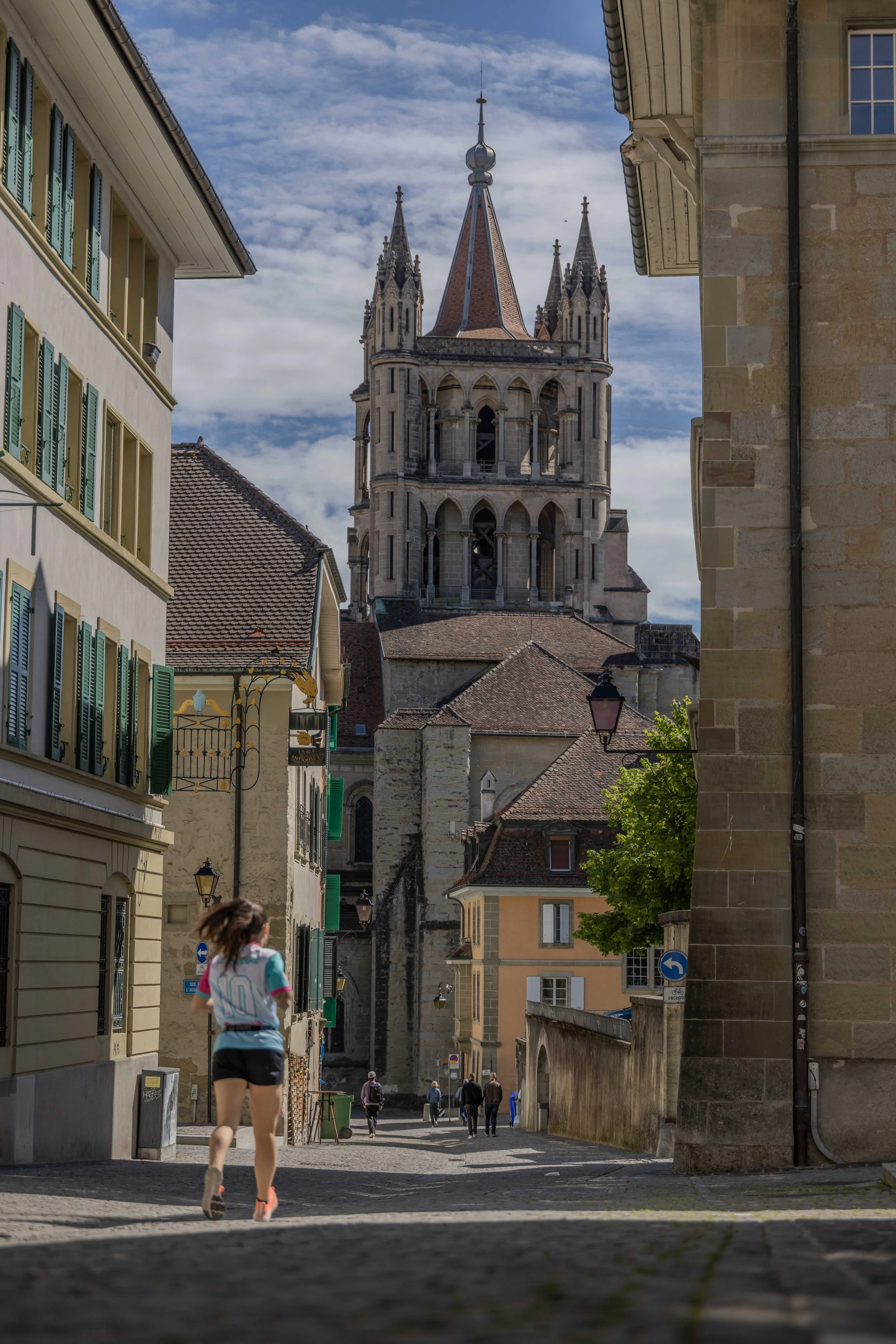 Une rue pavée dans une ville européenne avec des bâtiments anciens et une église en arrière-plan, un groupe de personnes marchent et une fille en course dans la rue.