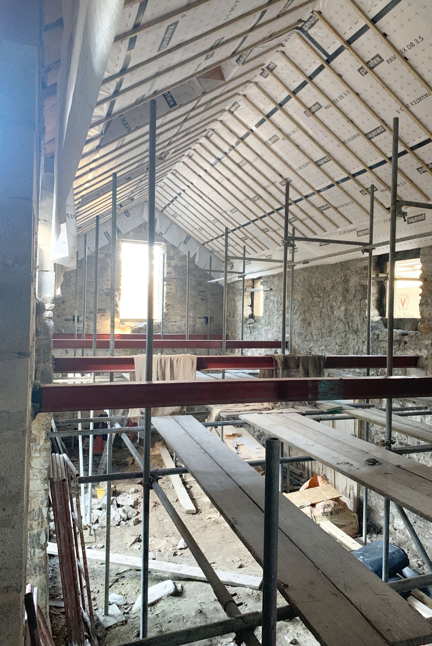 Site photograph of a barn conversion interior showing the bare construction materials of steel beams and timber framed roof with airtightness membrane visible