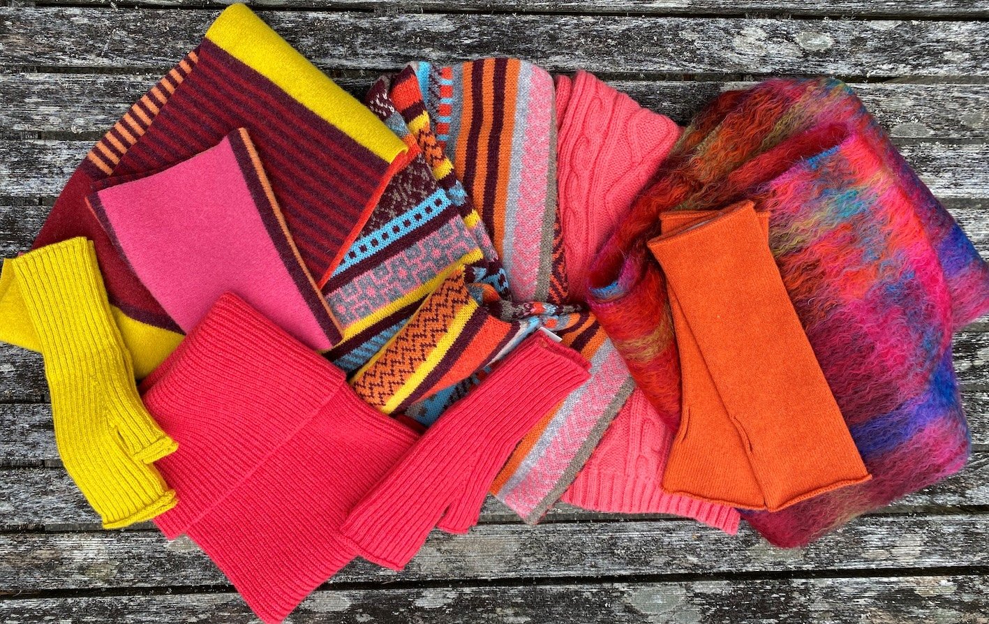 Colourful knitted and woolen accessories from Green Grove weavers, including hats, mittens, and scarves, with vibrant patterns and stripes, laid on a wooden surface.